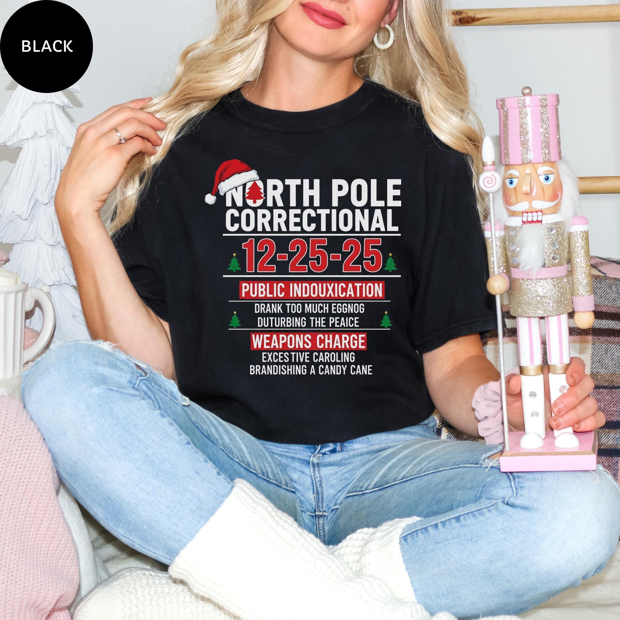 A woman wearing a black t-shirt with a humorous Christmas-themed design, sitting on a couch and holding a nutcracker.