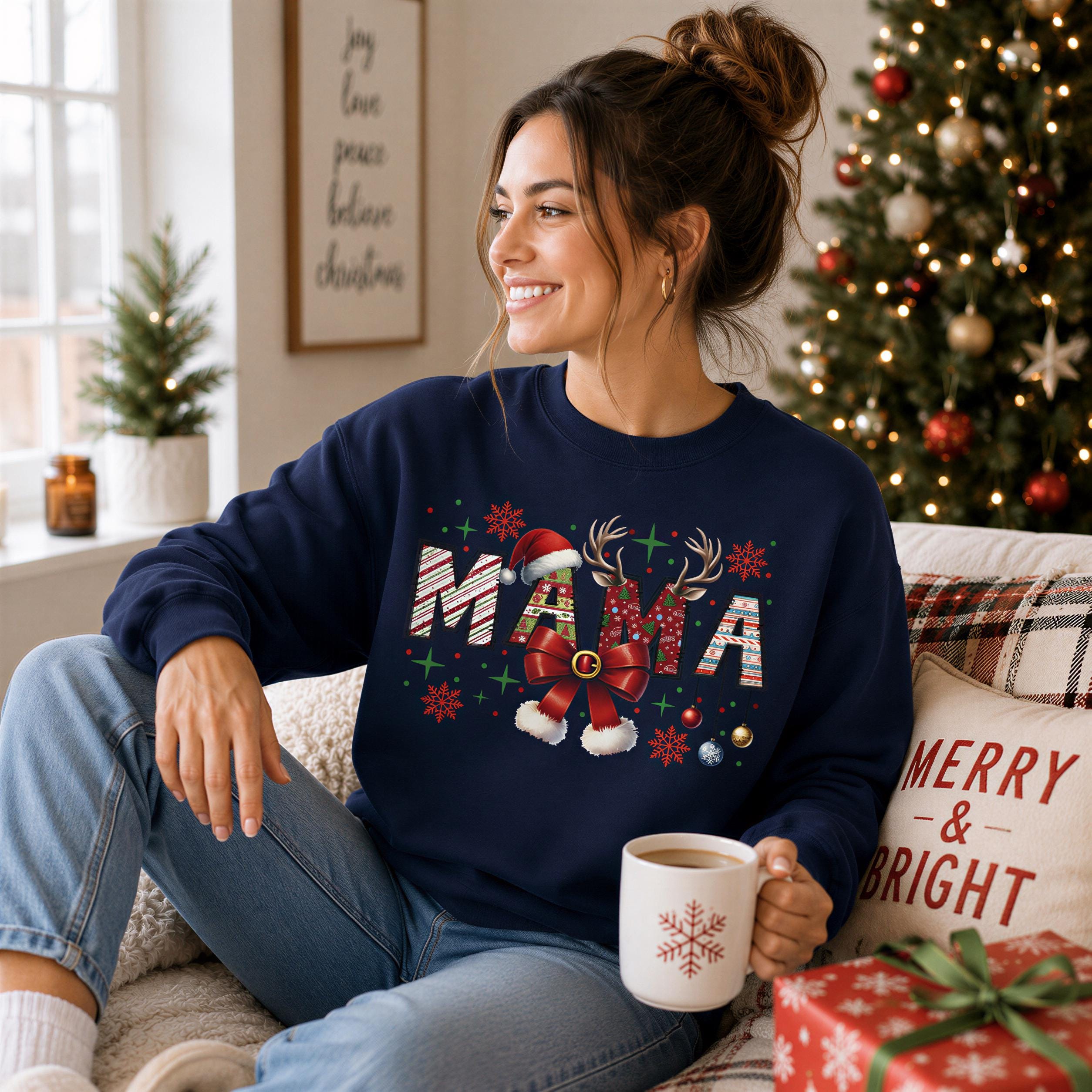 A woman sitting on a couch wearing a blue sweatshirt with the word "MAMA" printed on it, smiling and holding a coffee mug.