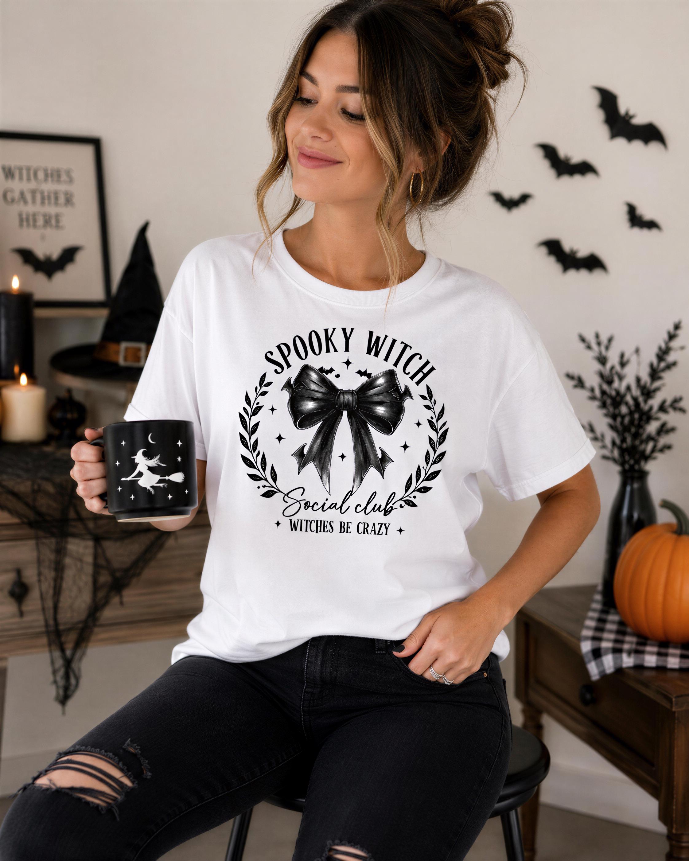 A woman wearing a white t-shirt with a graphic design and text, sitting on a stool and holding a mug.