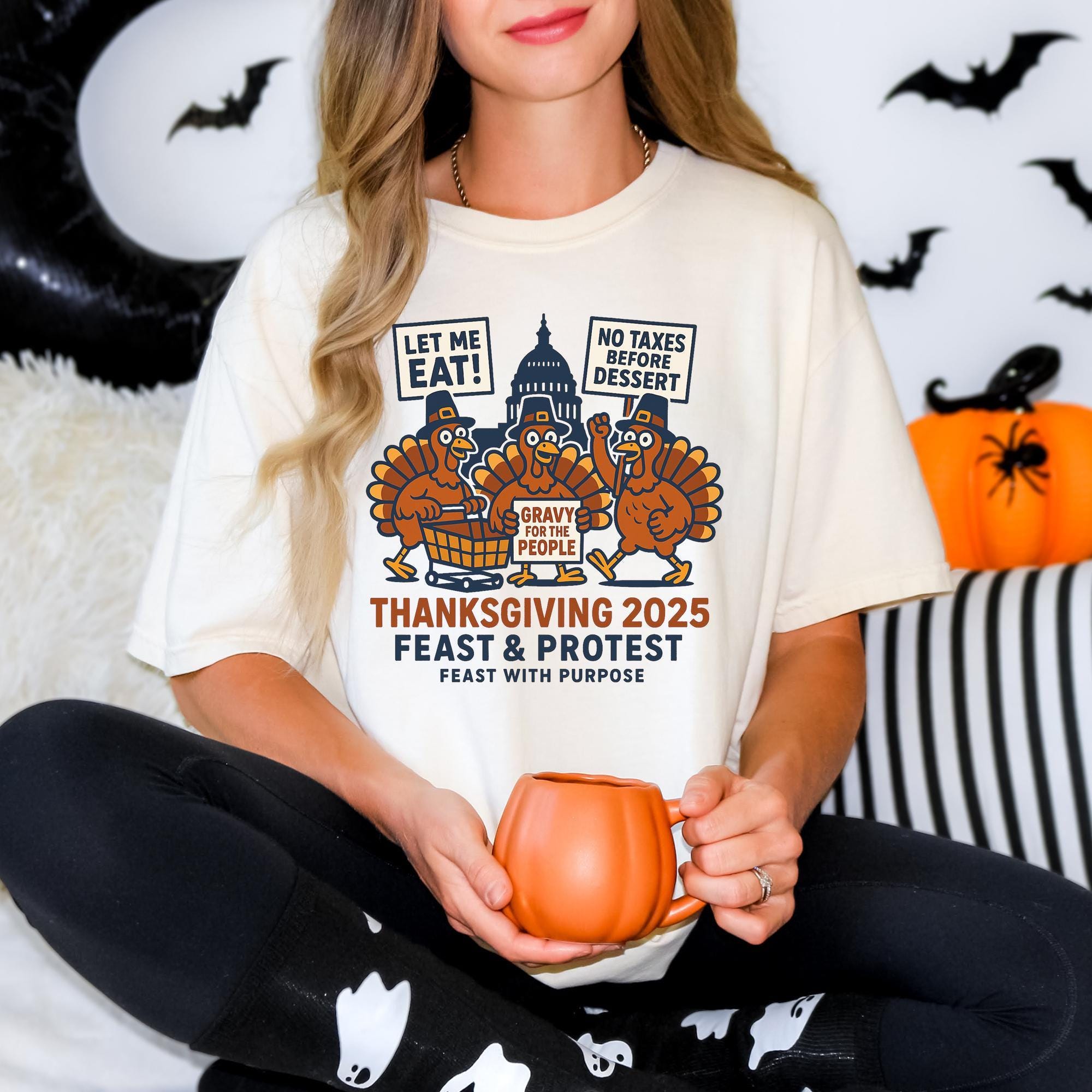 A woman wearing a white t-shirt with a graphic design of three cartoon turkeys and a message about Thanksgiving 2025. She is holding a pumpkin-shaped mug and appears to be sitting on a couch.