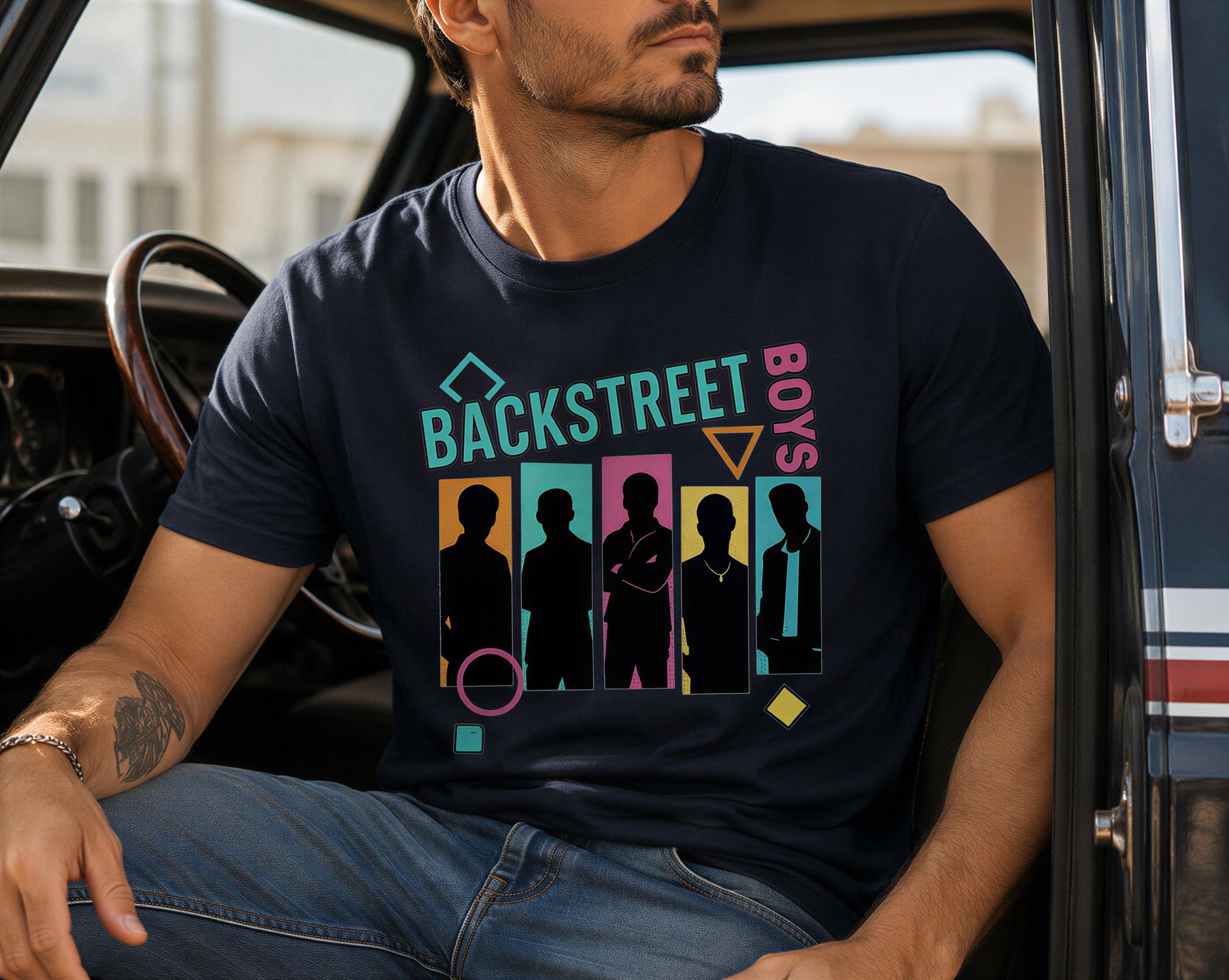A man wearing a black t-shirt with a graphic design featuring silhouettes of five people and the text "BACKSTREET BOYS" printed on it.