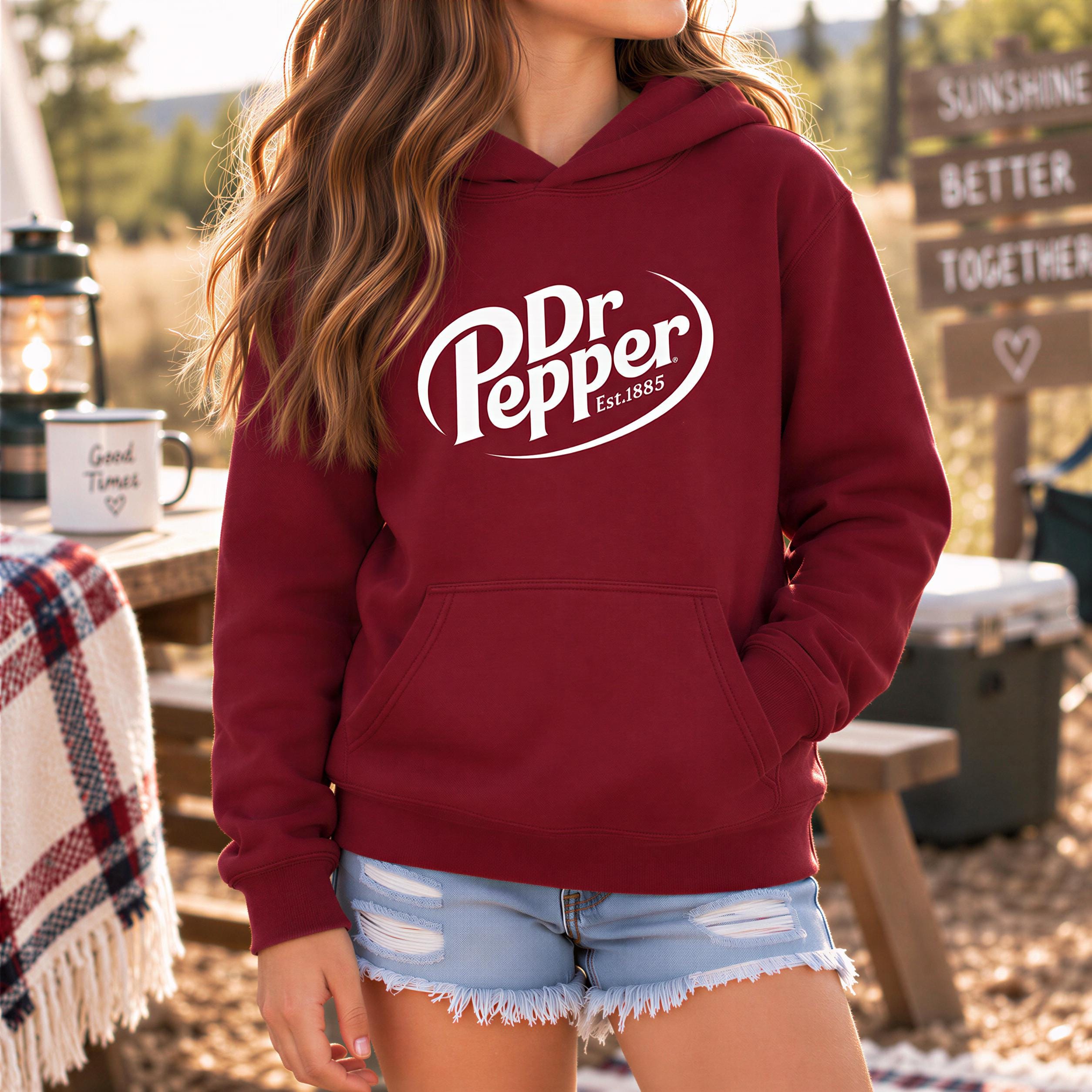 A woman wearing a red hoodie with the Dr Pepper logo stands outdoors, with a picnic table and a lantern visible in the background.