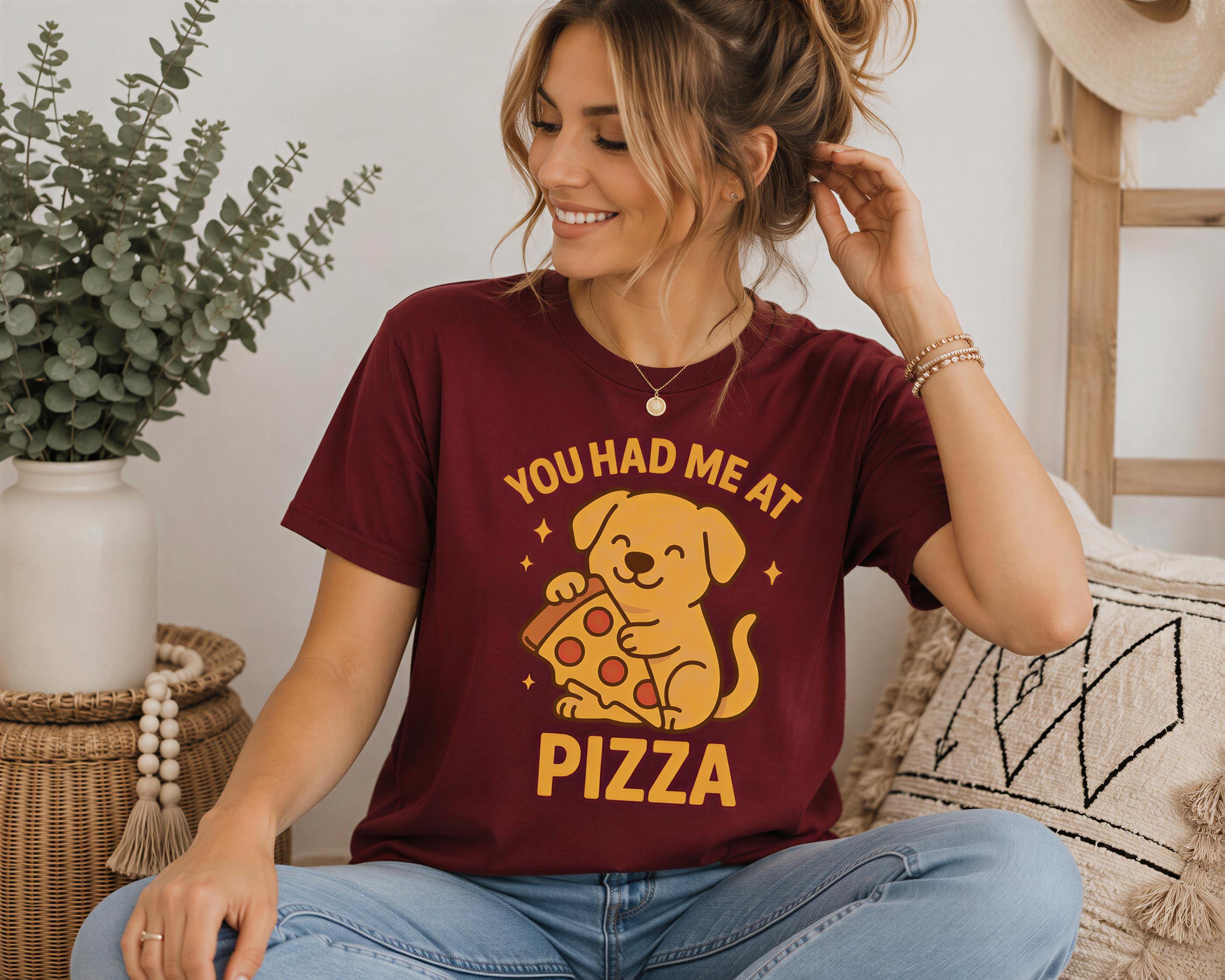 A woman wearing a maroon t-shirt with a cartoon dog holding a pizza slice and the text "YOU HAD ME AT PIZZA" is sitting on a couch.