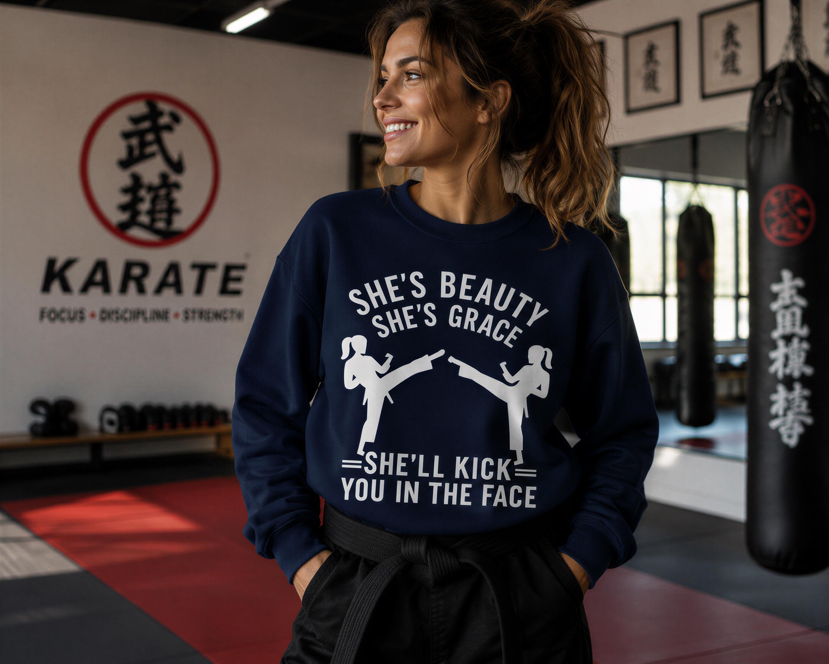A woman wearing a blue sweatshirt with a graphic design stands in a gym with a punching bag and a Karate logo visible in the background.
