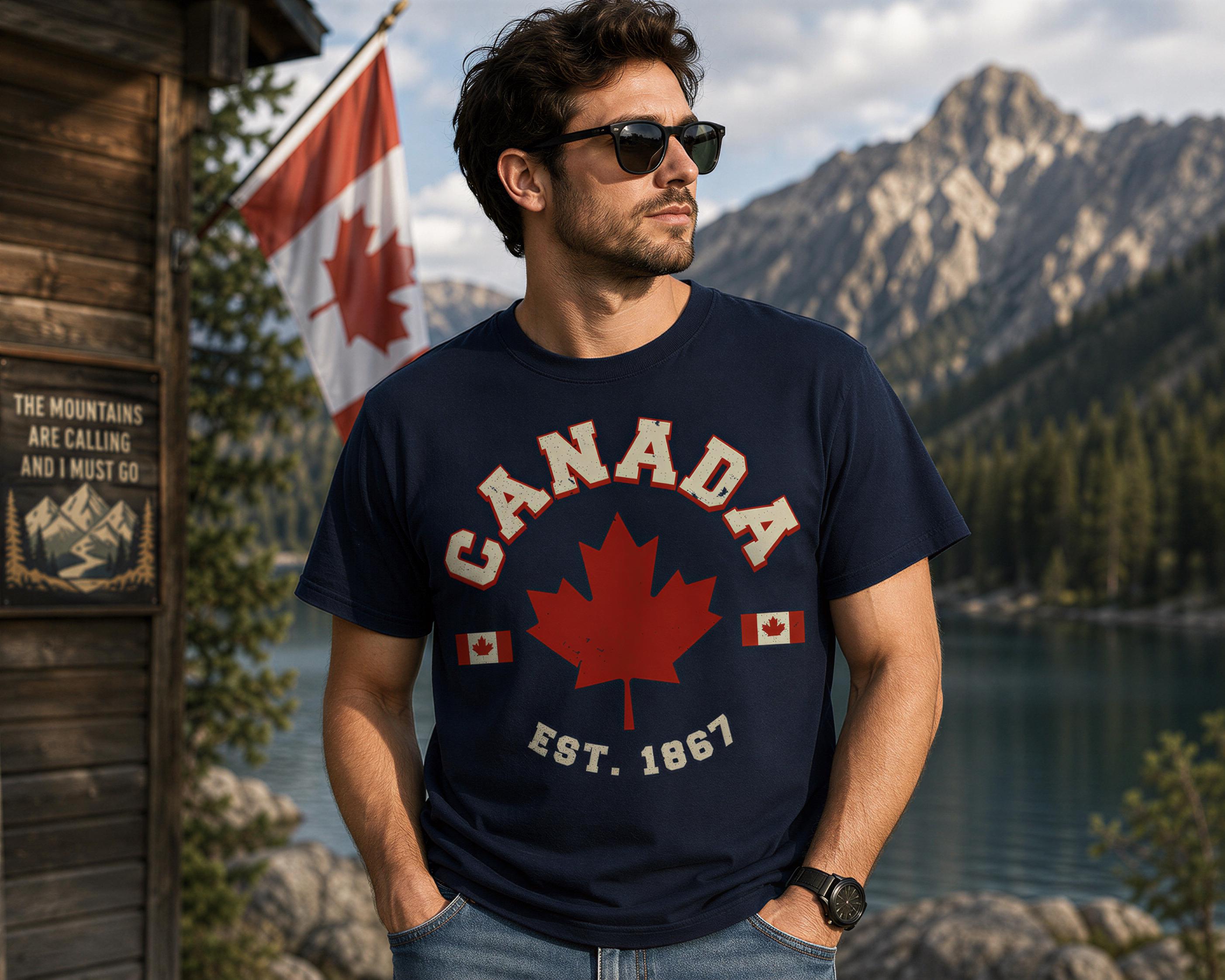 A man wearing a navy blue t-shirt with a red maple leaf and the words "CANADA" and "EST. 1867" stands in front of a wooden cabin with a mountain backdrop.