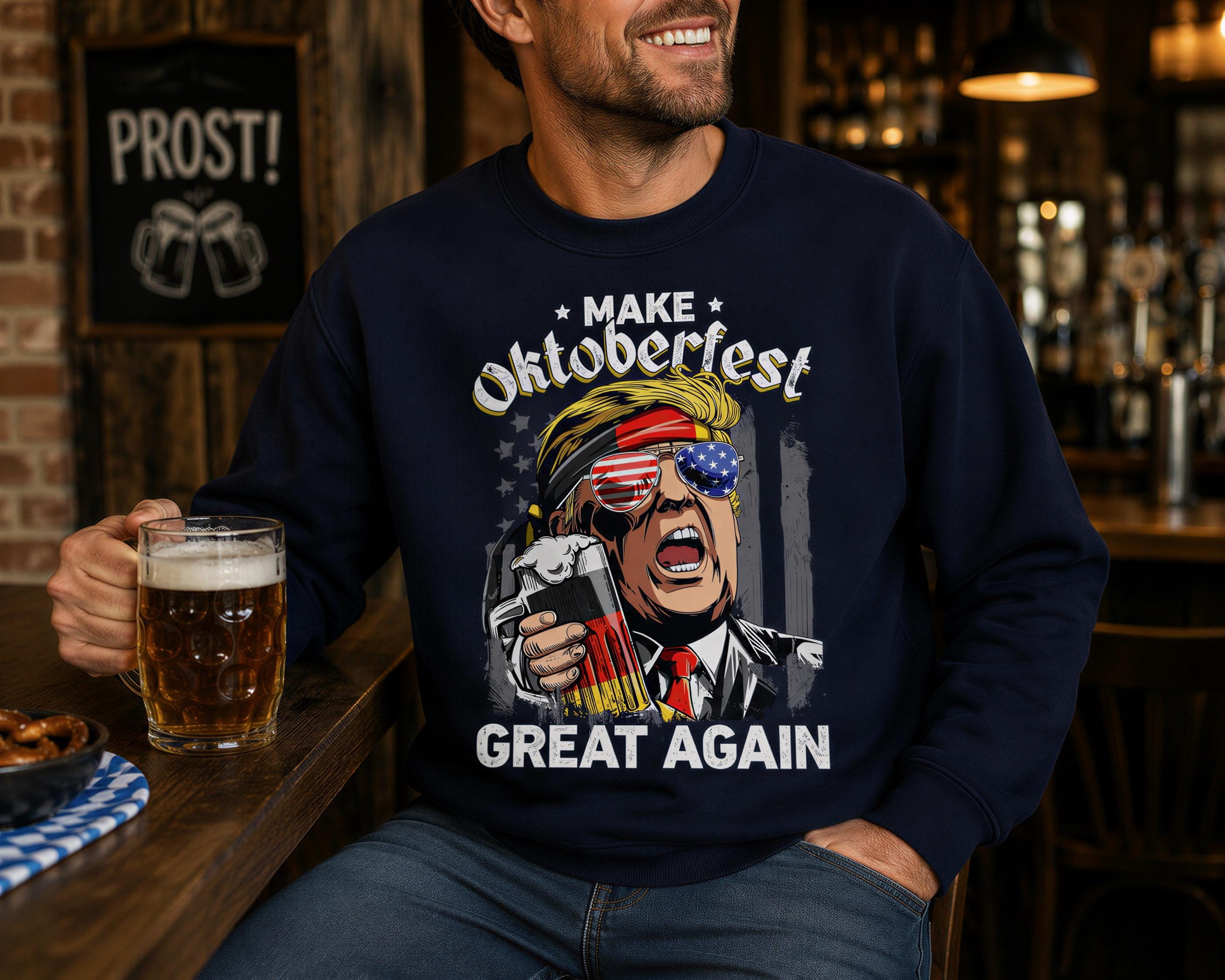 A man wearing a navy blue sweatshirt with a graphic of a man wearing sunglasses and holding a beer, sitting at a bar with a glass of beer in front of him.