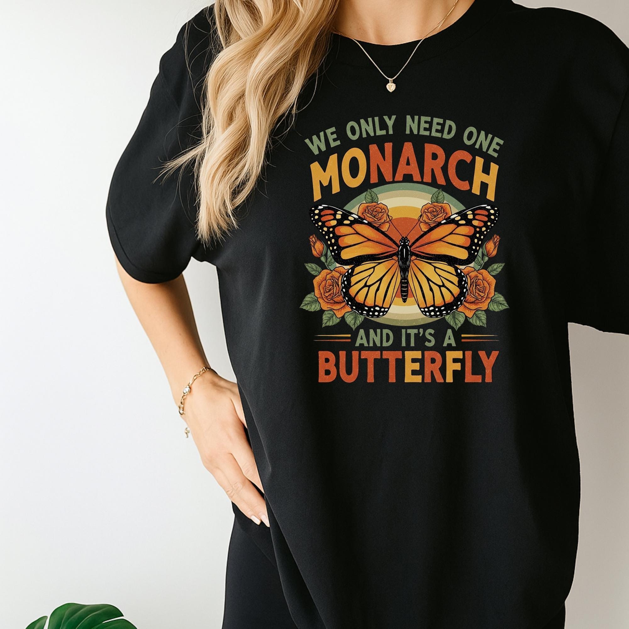 A person wearing a black t-shirt with a graphic design of a butterfly and the text "We only need one monarch and it's a butterfly" printed on it.