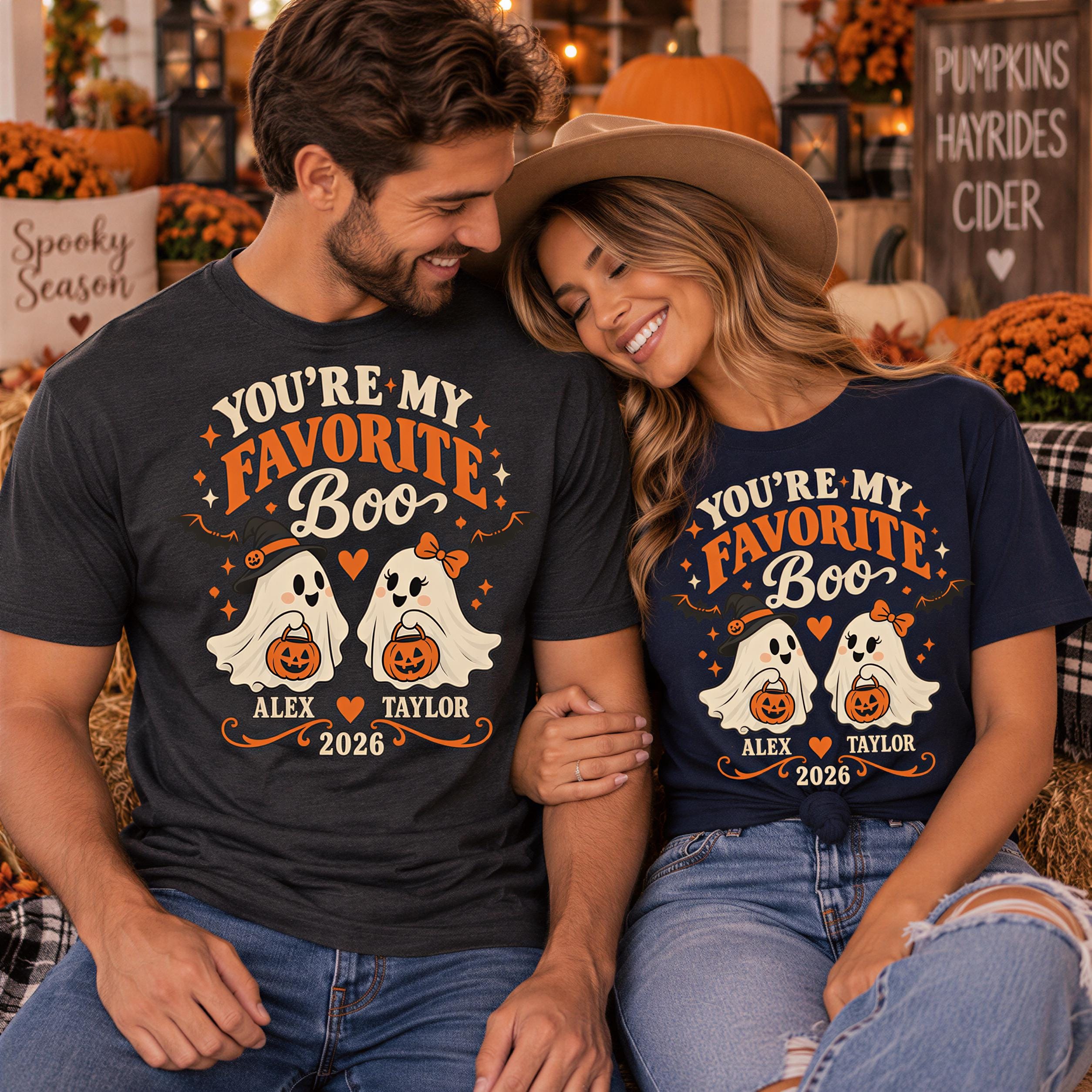 A man and a woman are sitting together, smiling and wearing matching t-shirts with a Halloween theme.