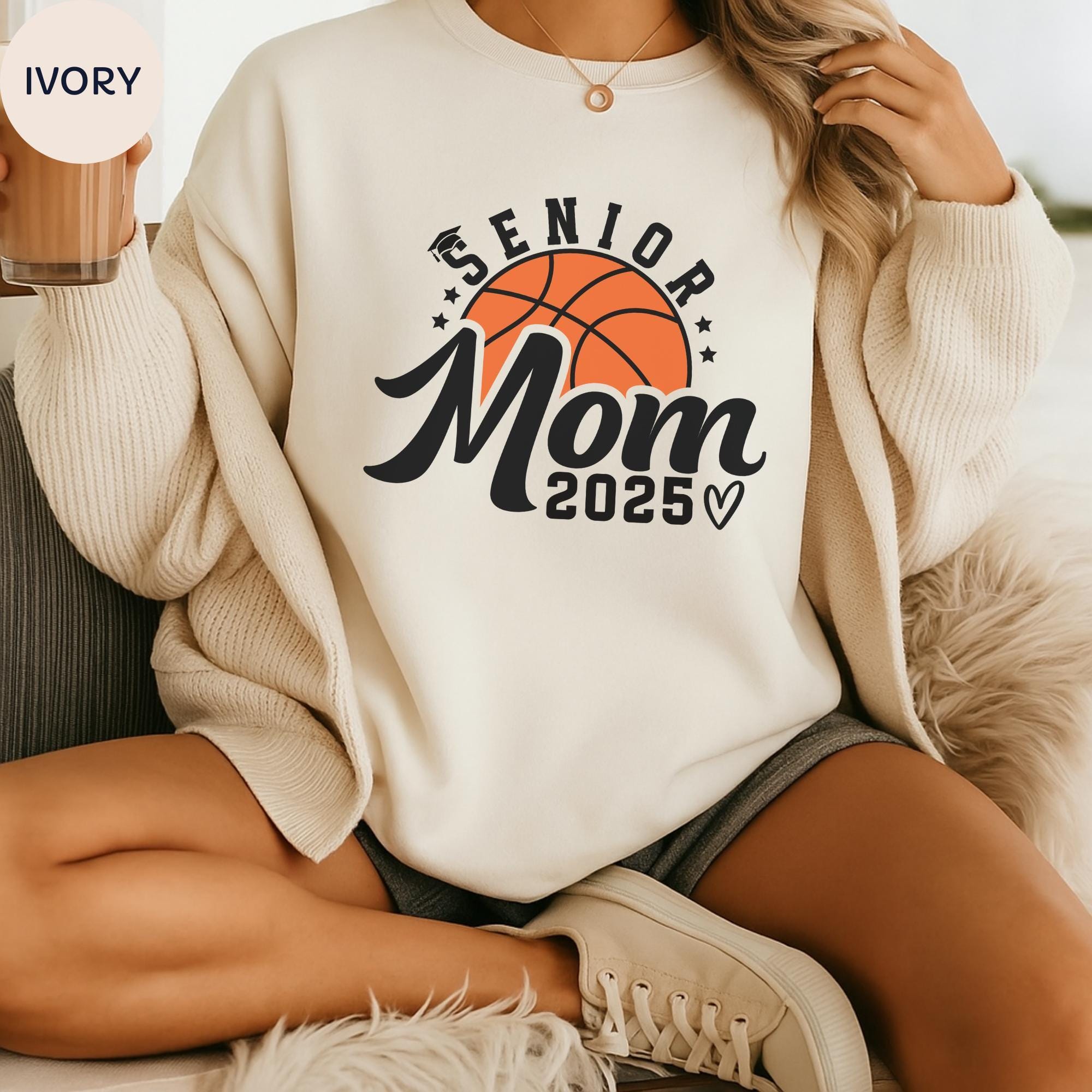 A person wearing a white sweatshirt with a basketball graphic and text that says "SENIOR MOM 2005" is sitting on a couch.