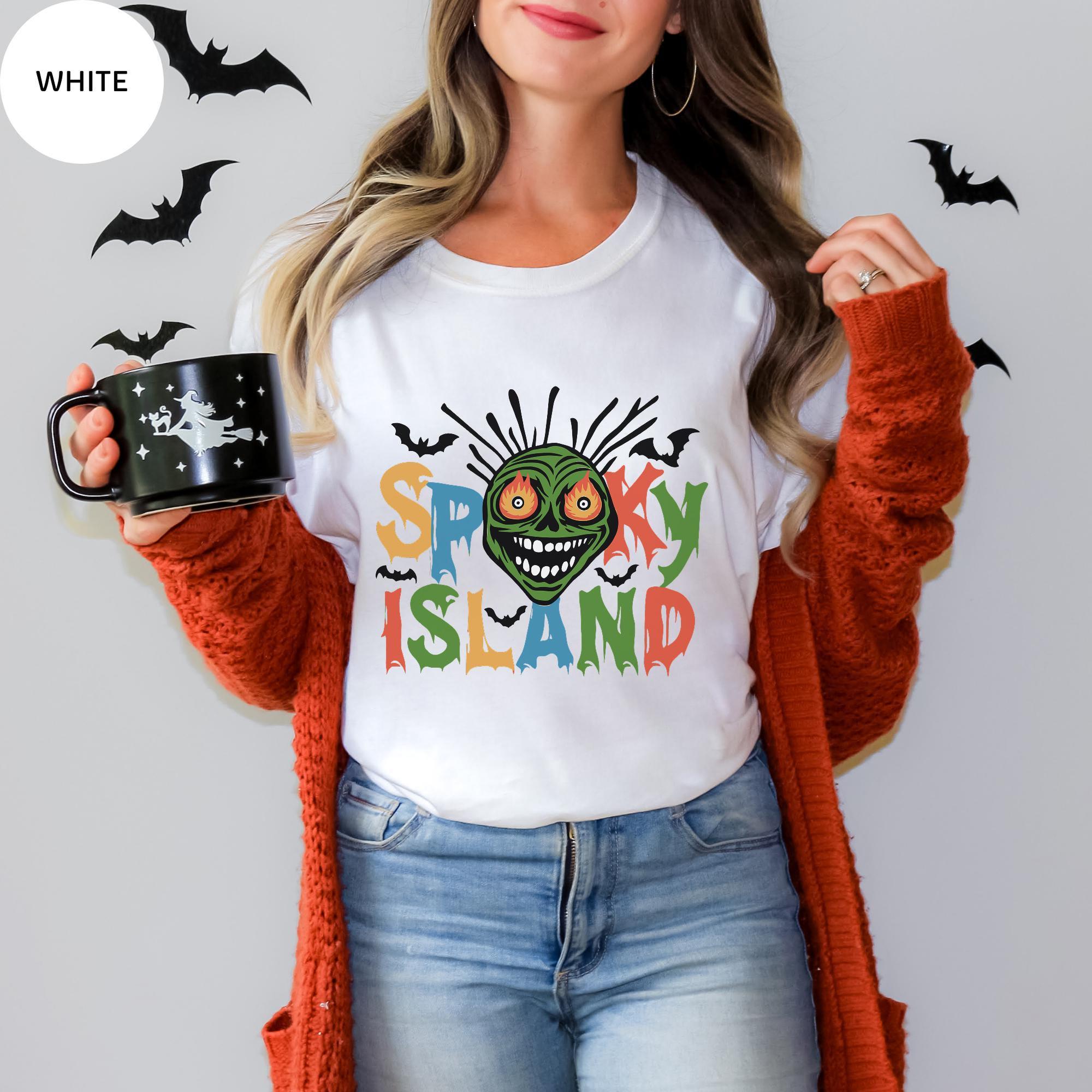 A woman wearing a white t-shirt with a graphic design of a spooky island and holding a mug with a black design.