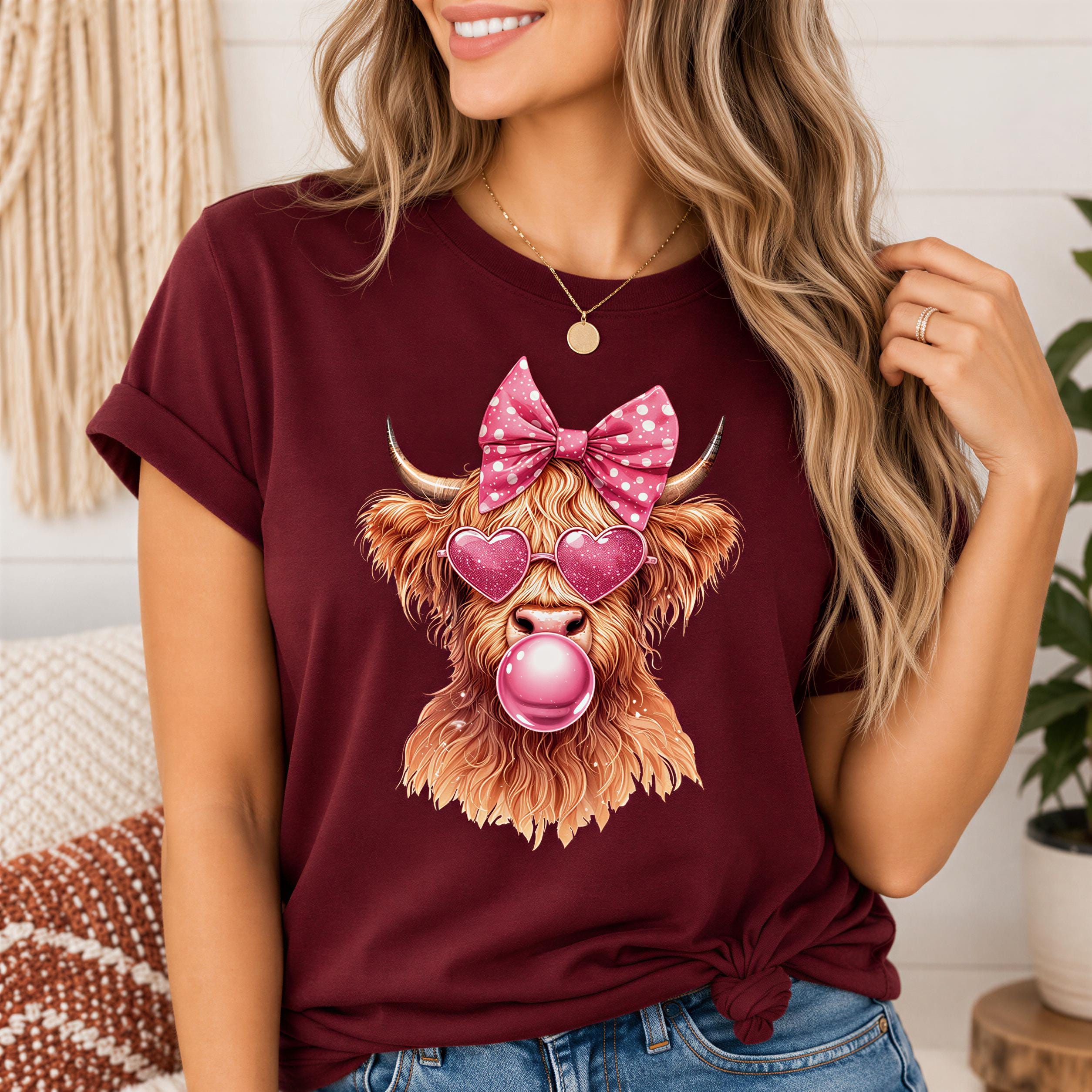 A woman wearing a burgundy t-shirt with a graphic of a cow wearing sunglasses and a pink bow.