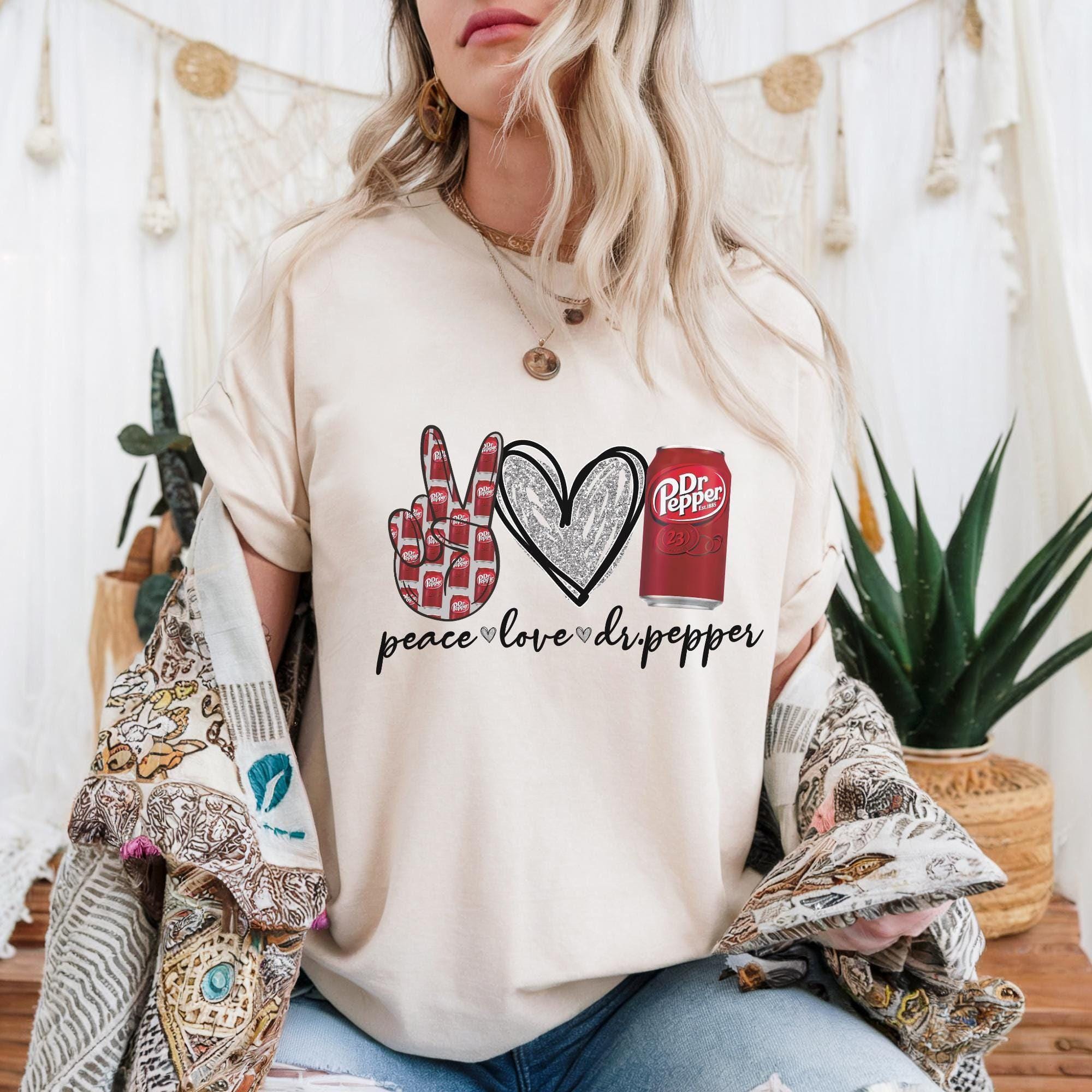 A woman wearing a white t-shirt with a peace sign graphic and text, sitting in front of a white background with plants and a woven basket.