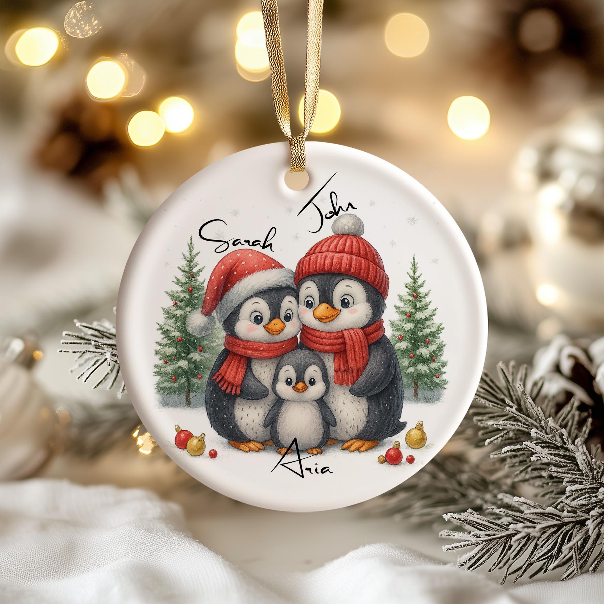 A white ornament with a family of three penguins, including a baby penguin, is hanging on a Christmas tree.