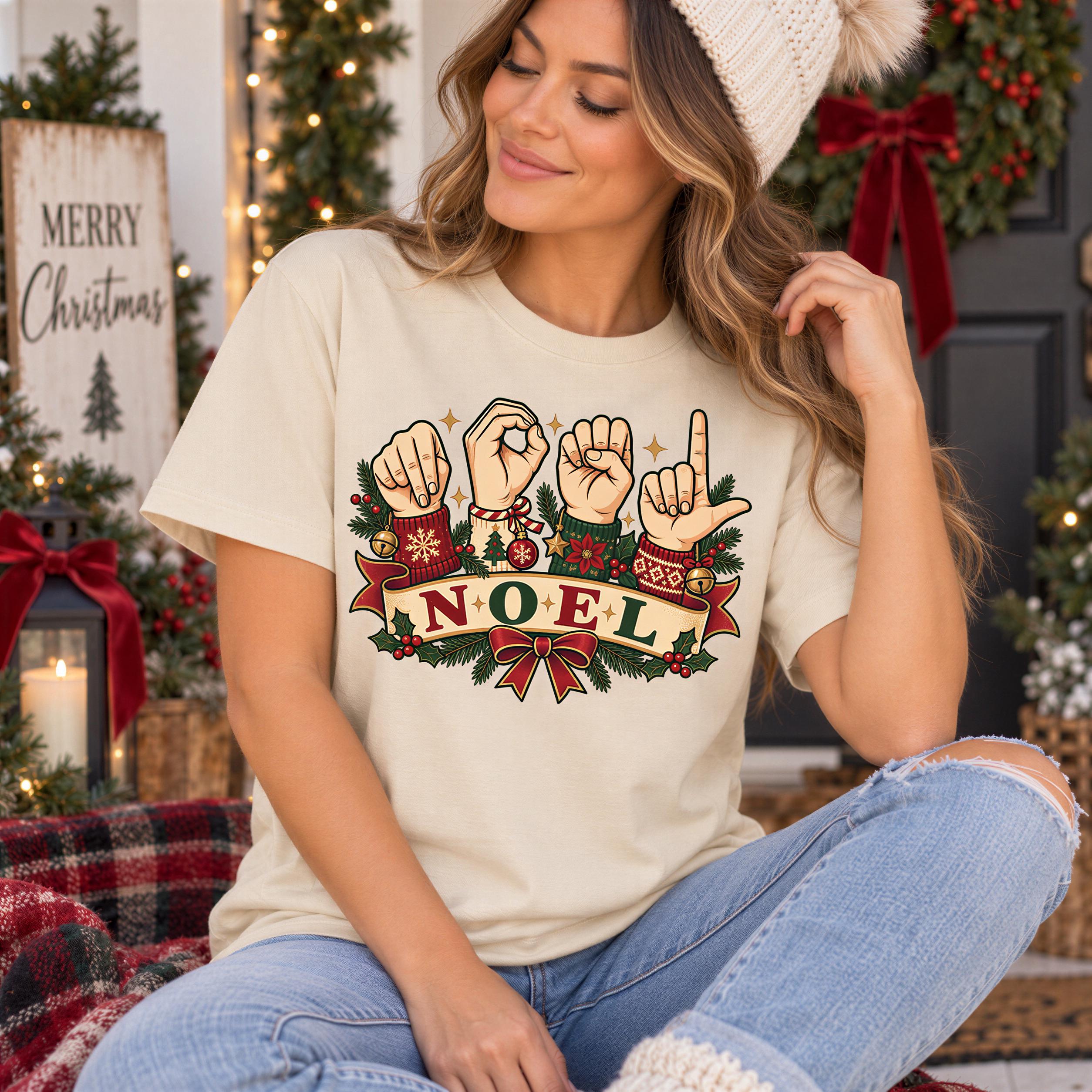 A woman wearing a white beanie and a t-shirt with a graphic design of the word " Noel" in a sign language style, sitting in front of a Christmas wreath.