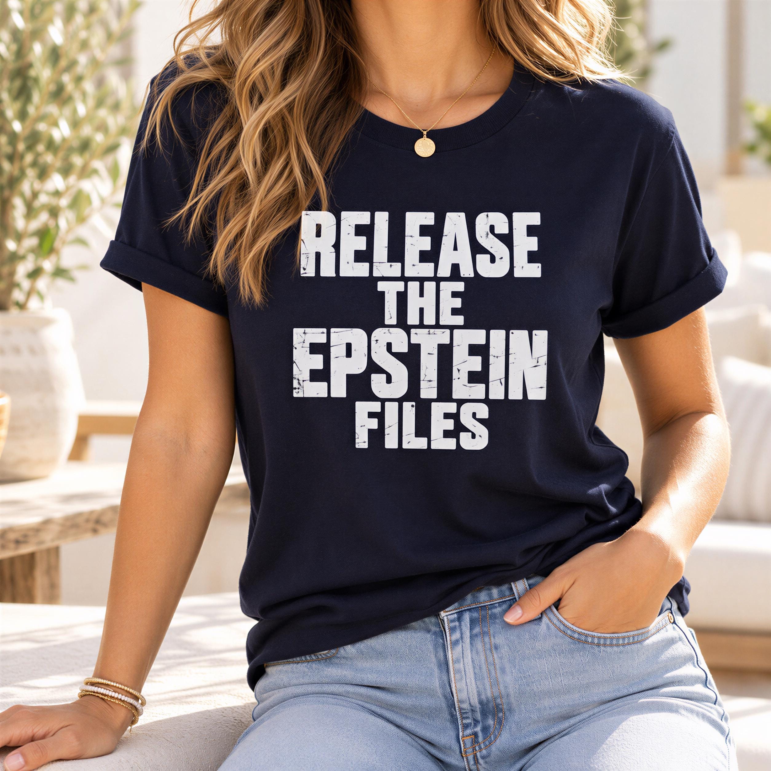 A woman wearing a navy blue t-shirt with the text "RELEASE THE EPSTEIN FILES" printed on it.