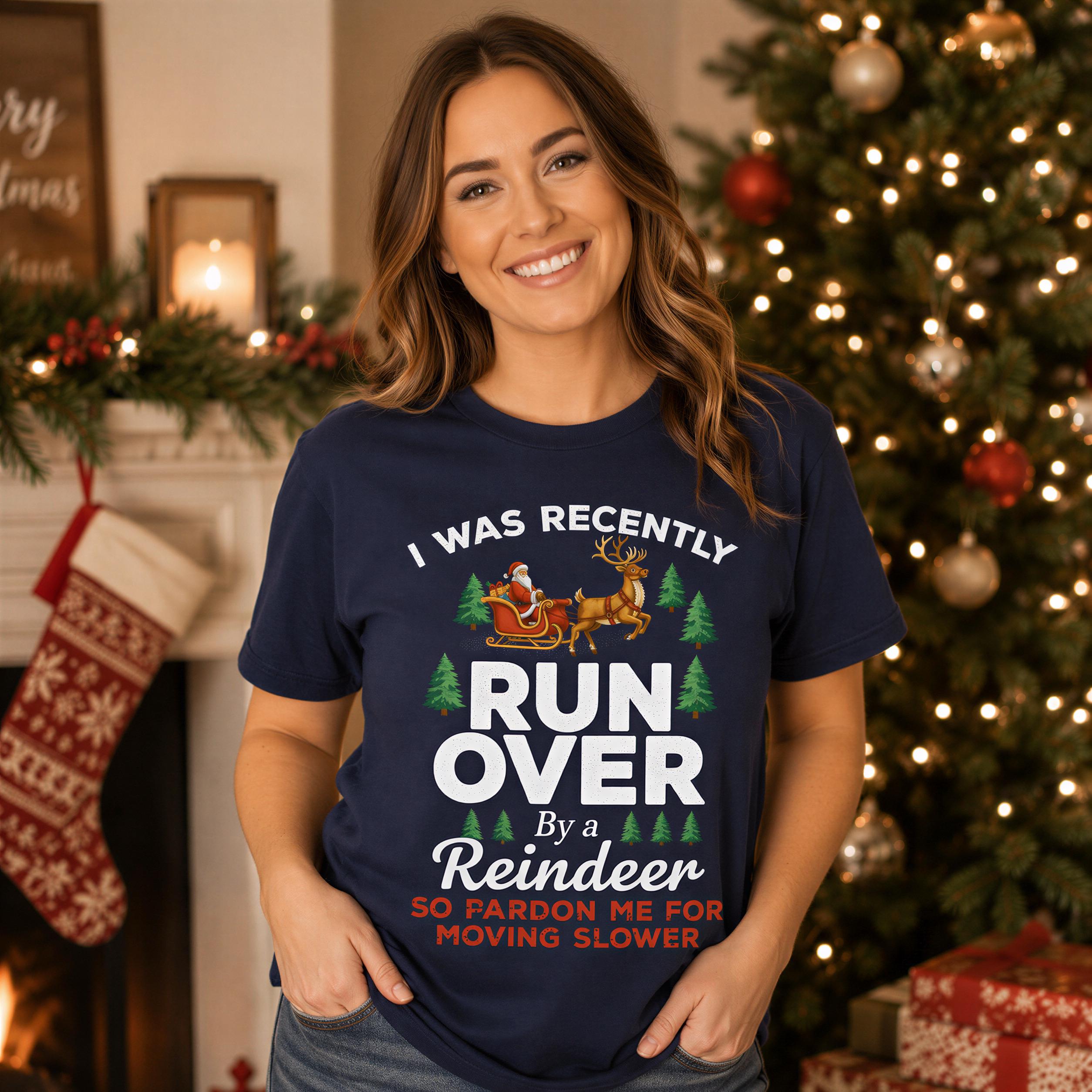 A woman wearing a navy blue t-shirt with a humorous Christmas-themed design, smiling and posing in front of a Christmas tree.