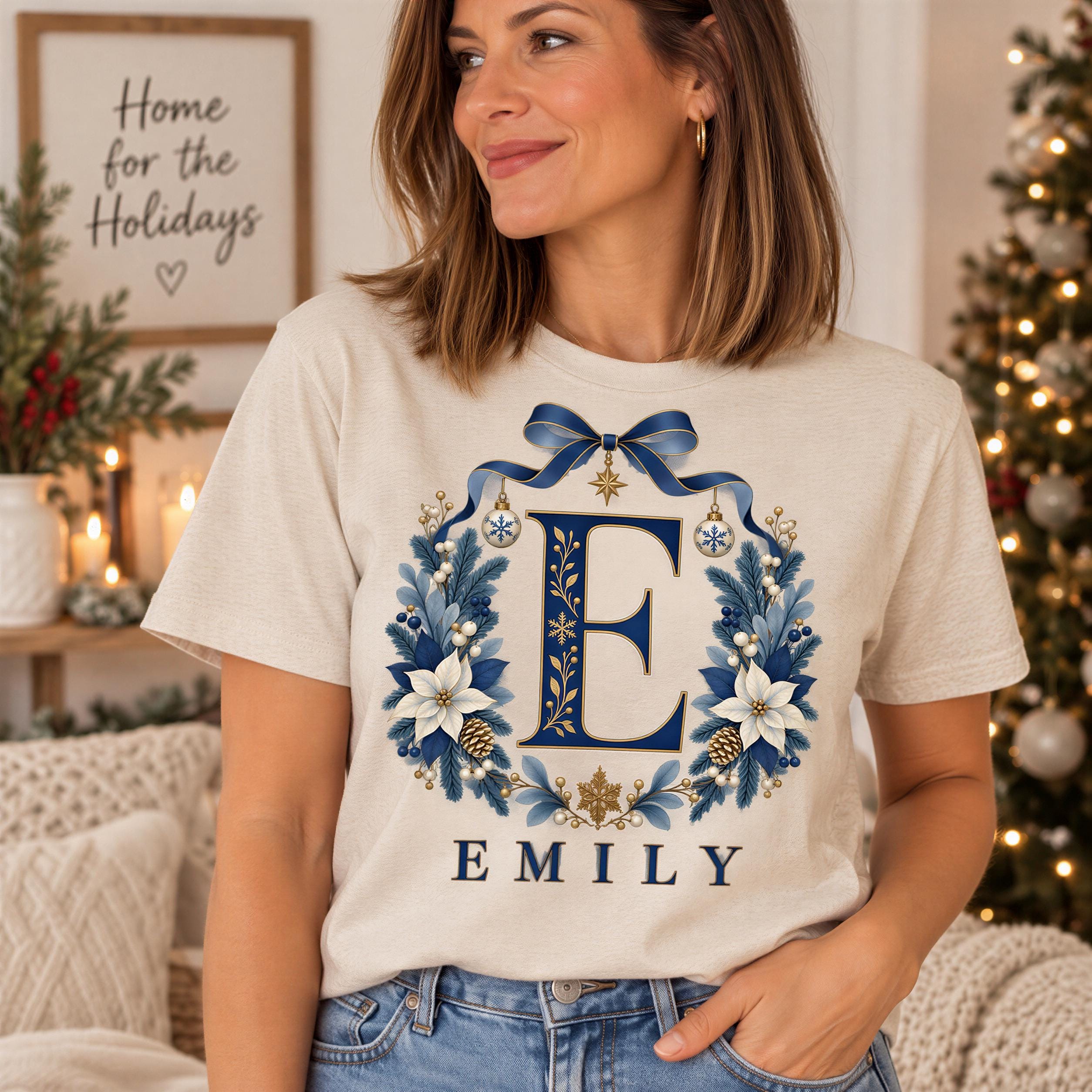 A woman wearing a beige t-shirt with a floral design and the name "EMILY" printed on it, standing in front of a Christmas tree.