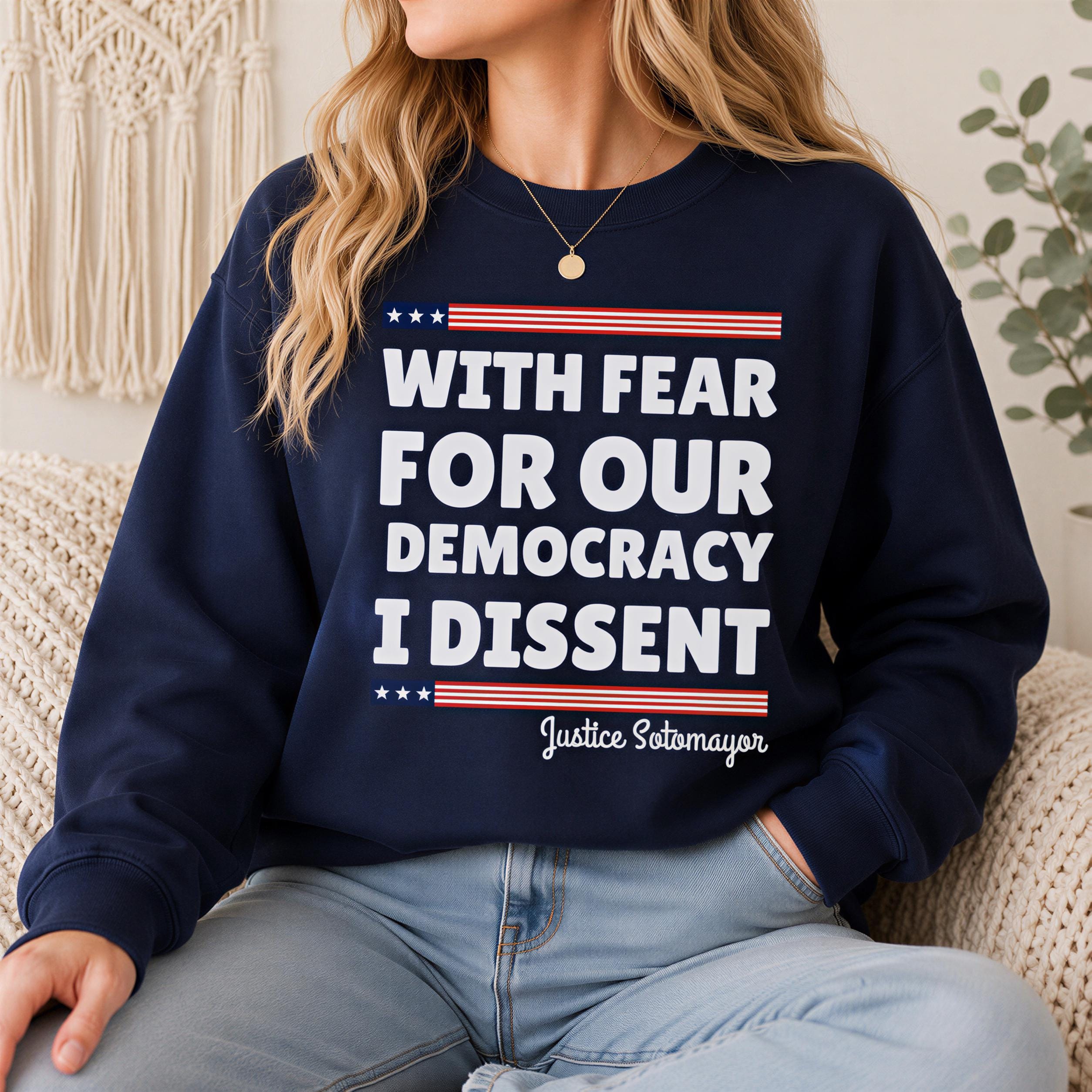 A woman wearing a navy blue sweatshirt with the text "With fear for our democracy I dissent" printed on it.