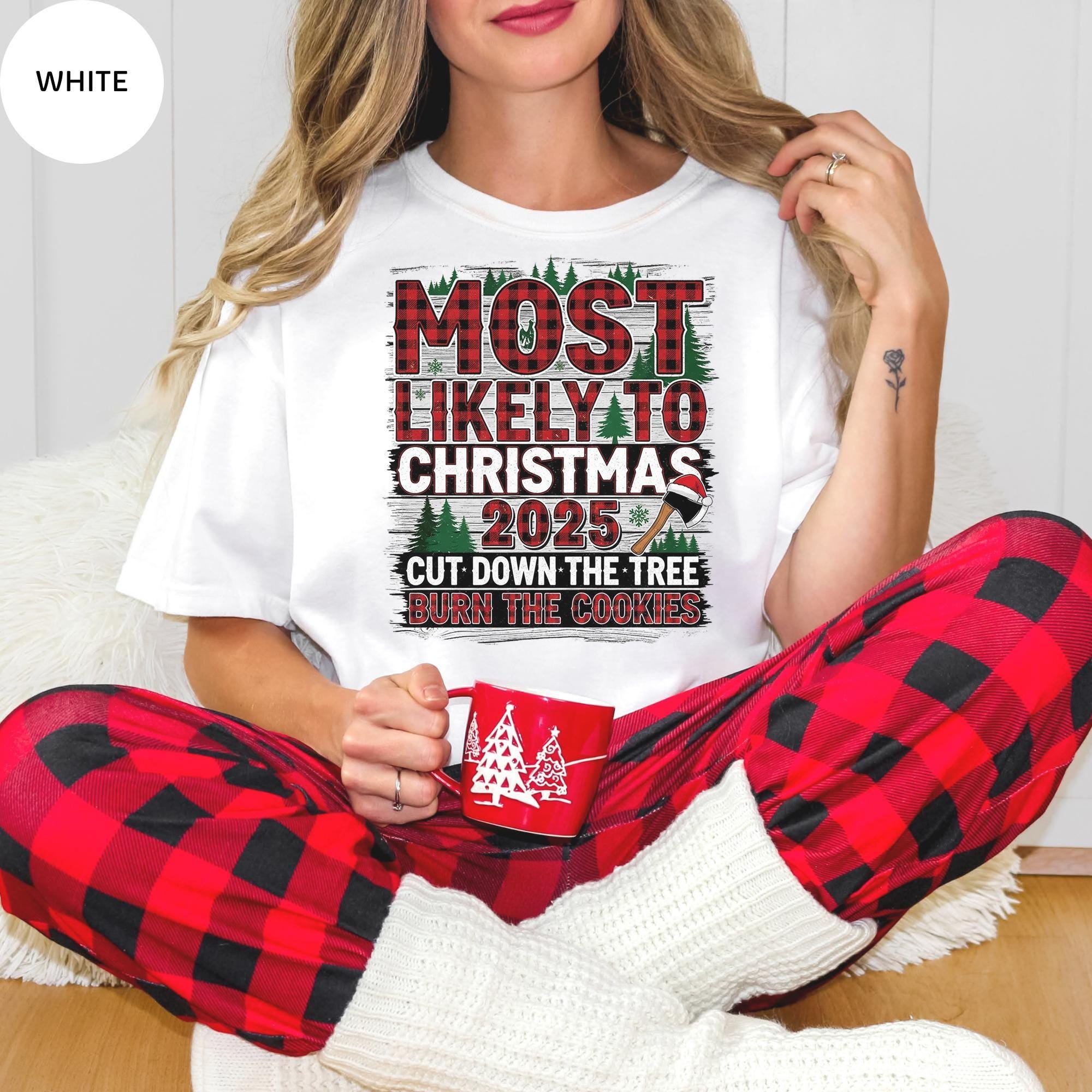 A woman wearing a white t-shirt with a humorous Christmas-themed design, sitting on the floor and holding a mug.
