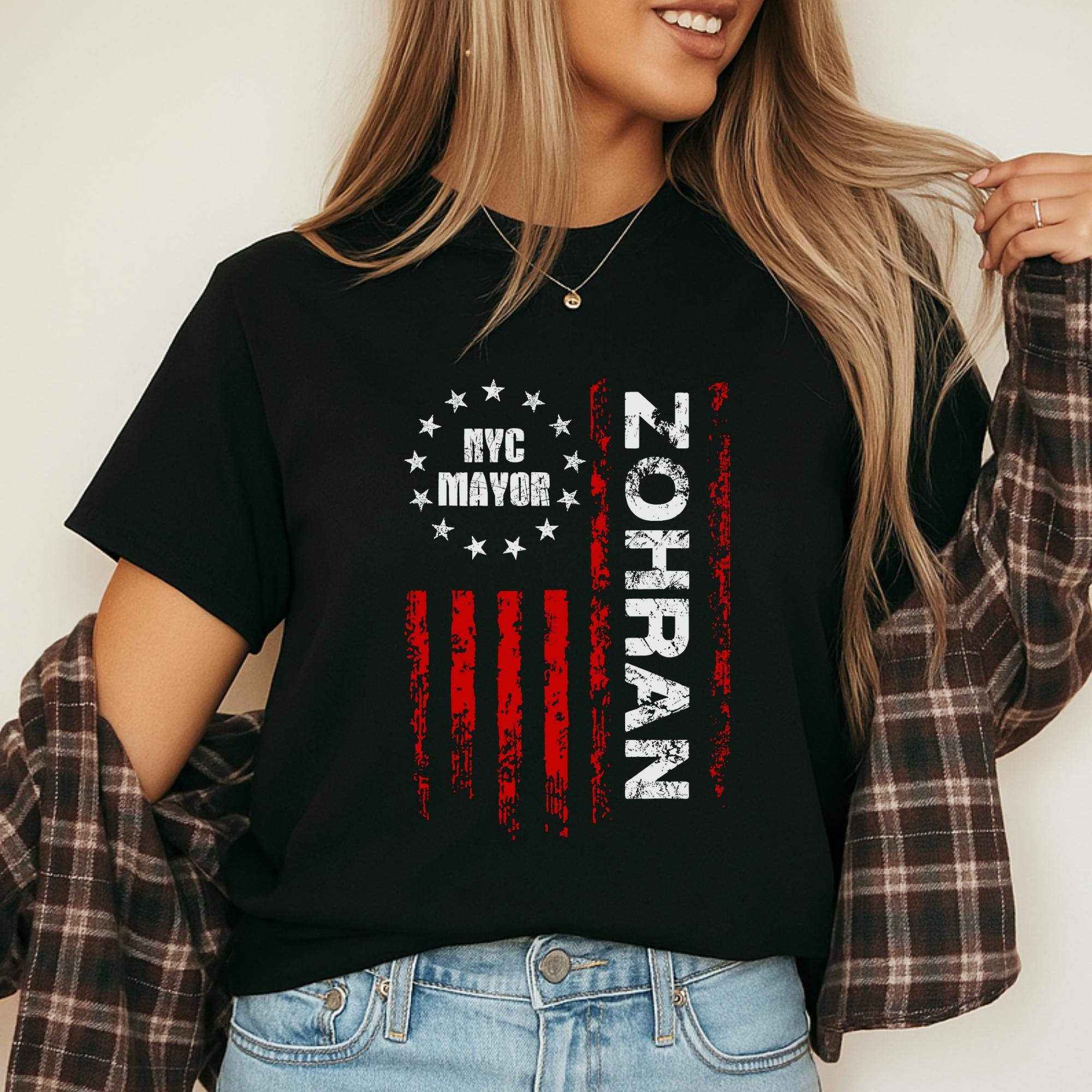 A woman wearing a black t-shirt with a graphic design featuring a red and white striped flag and the text "NYC MAYOR ZOHRAN" printed on it.