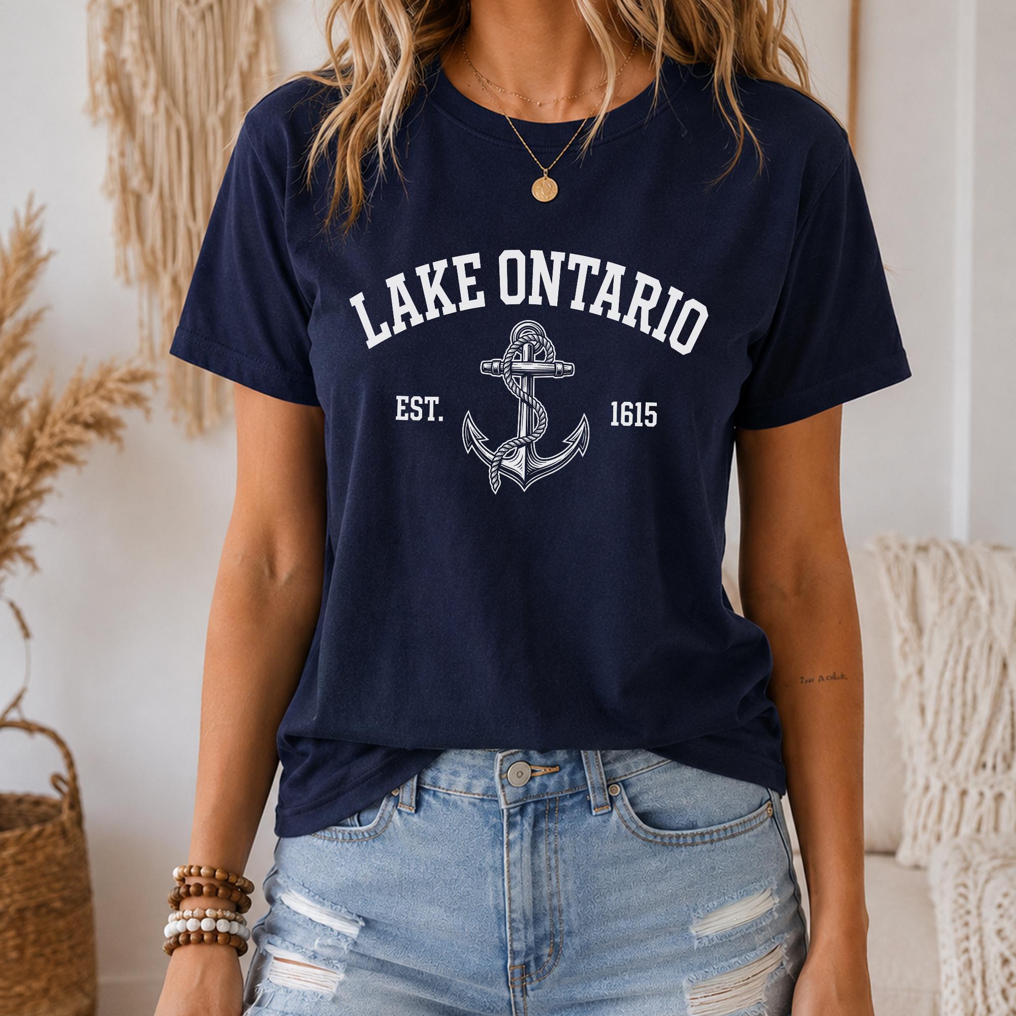 A woman wearing a navy blue t-shirt with the text "LAKETARIO EST. 1615" printed on it, along with an anchor graphic. She is also wearing denim shorts and has a necklace around her neck.