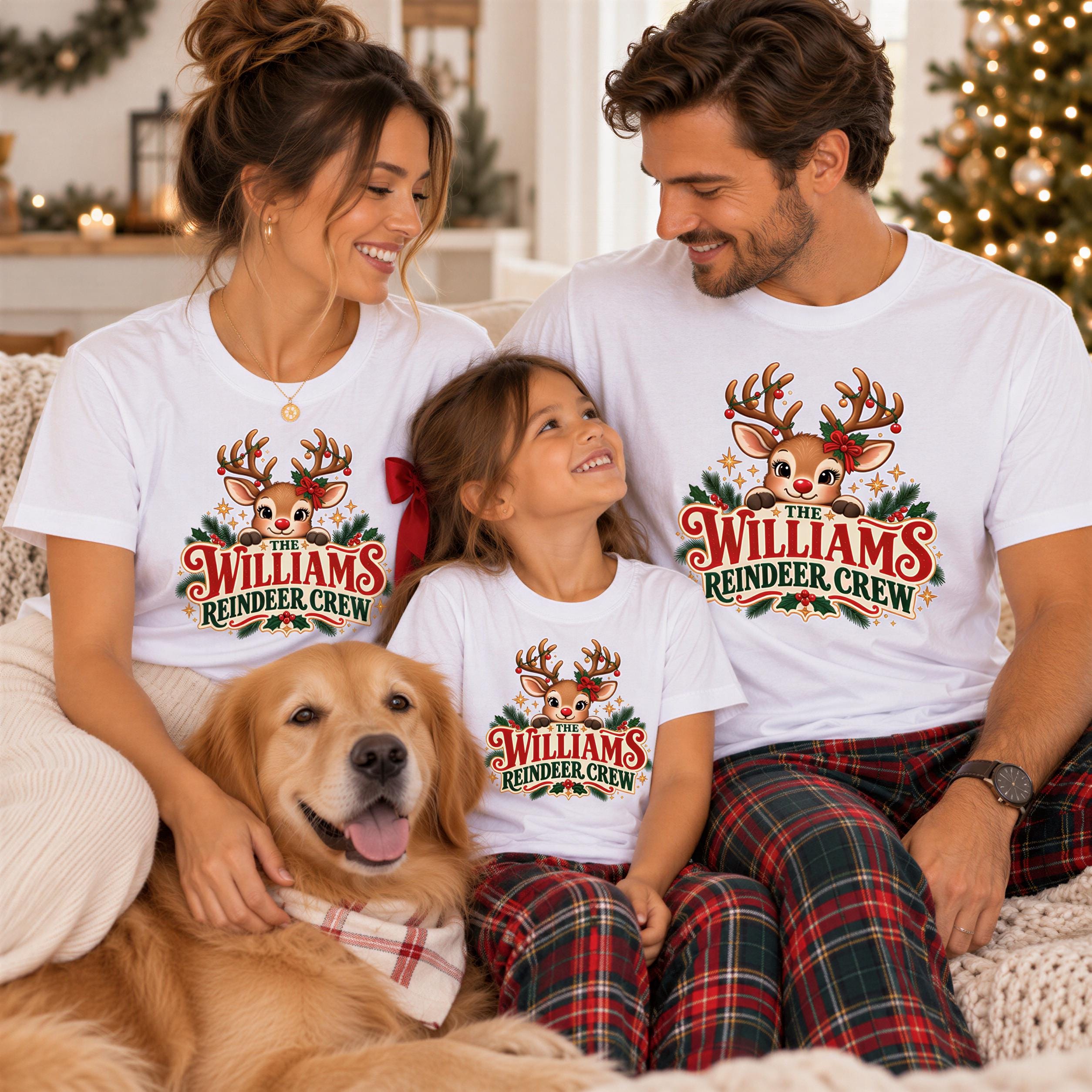 A family of three, consisting of a mother, father, and daughter, is sitting together on a couch with a dog. They are all wearing matching white t-shirts with a reindeer design and the text "The Williams Reindeer Crew".