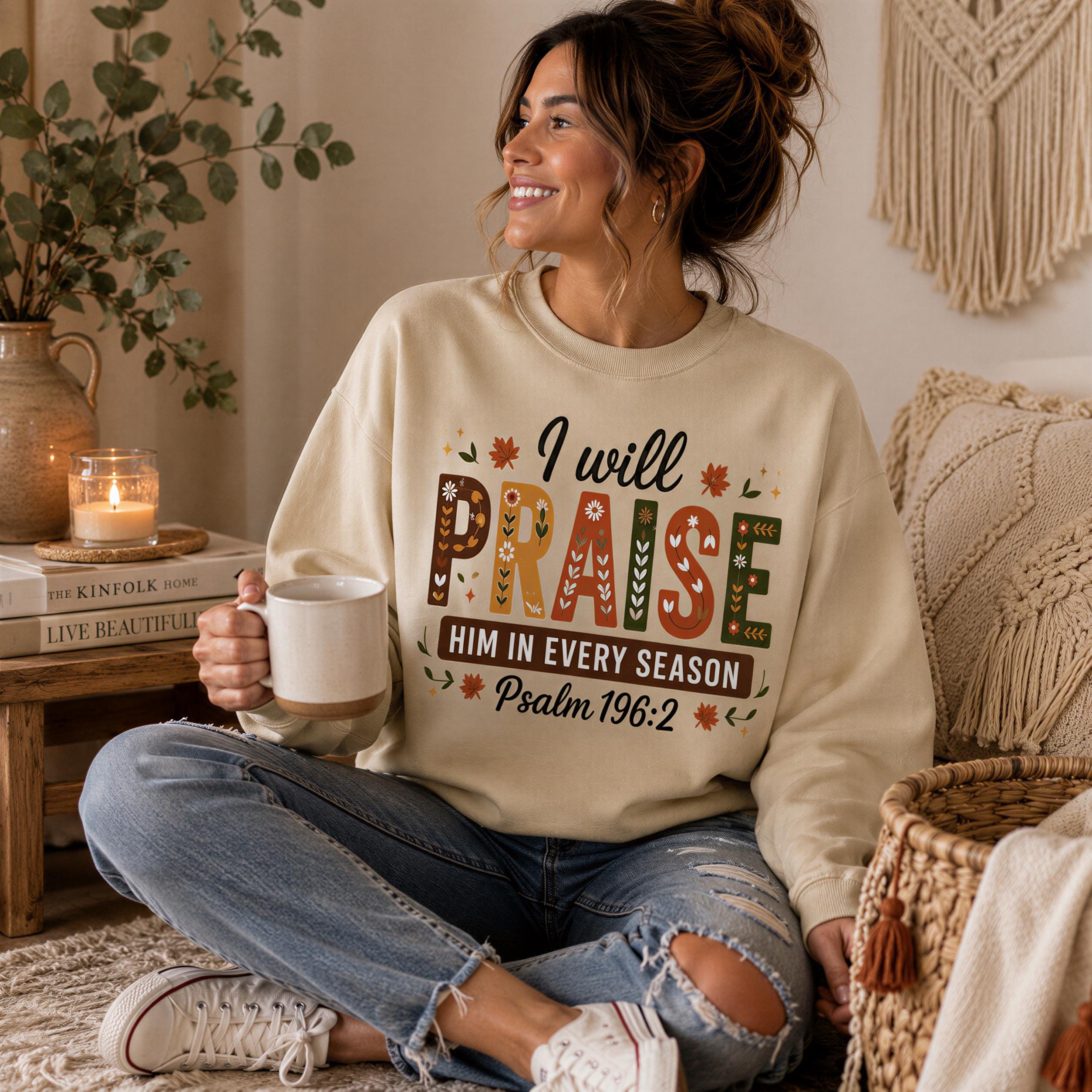 A woman sitting on the floor, wearing a sweatshirt with a message about praise and Him in every season, holding a mug and smiling.