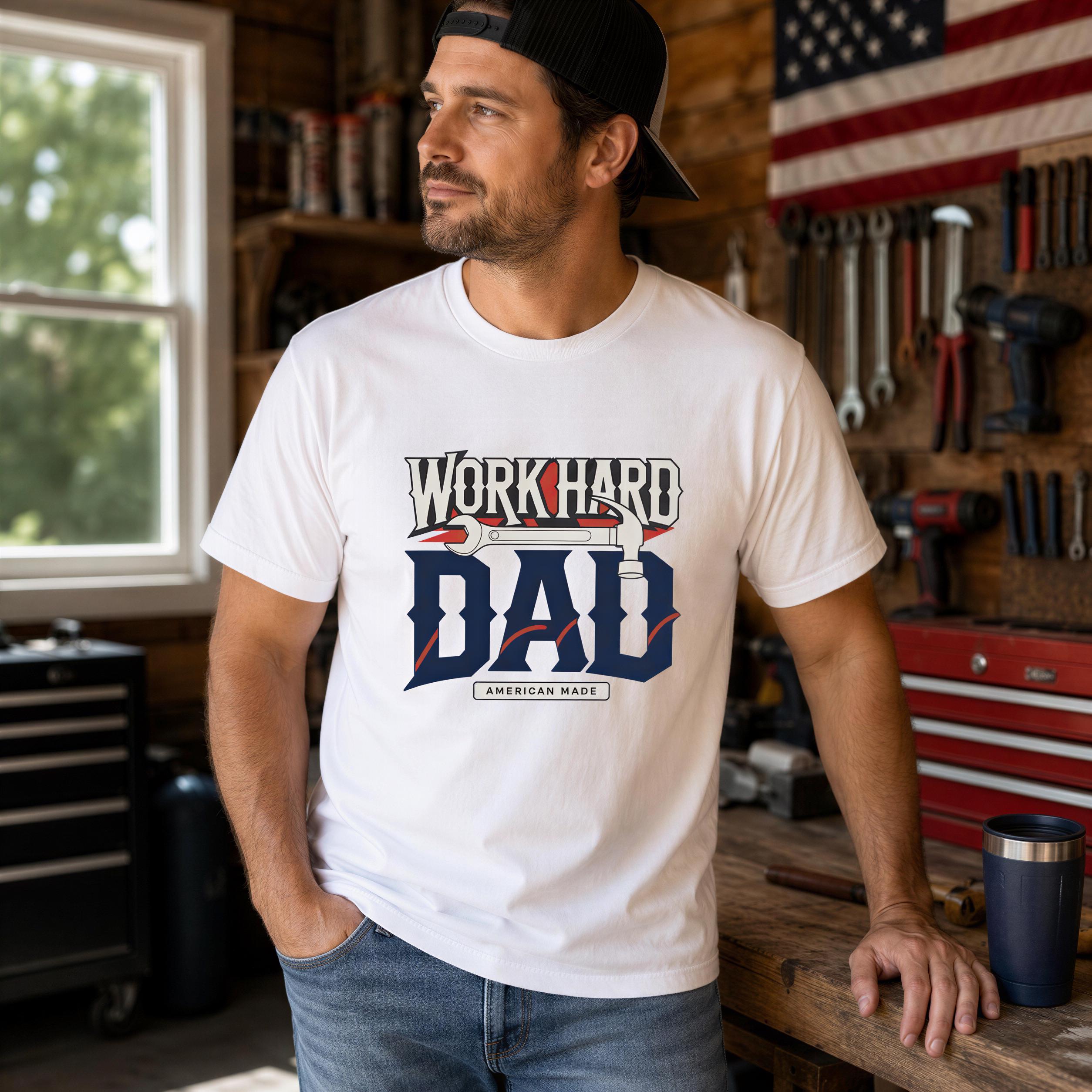 A man wearing a white t-shirt with a graphic design stands in a workshop surrounded by tools and equipment.