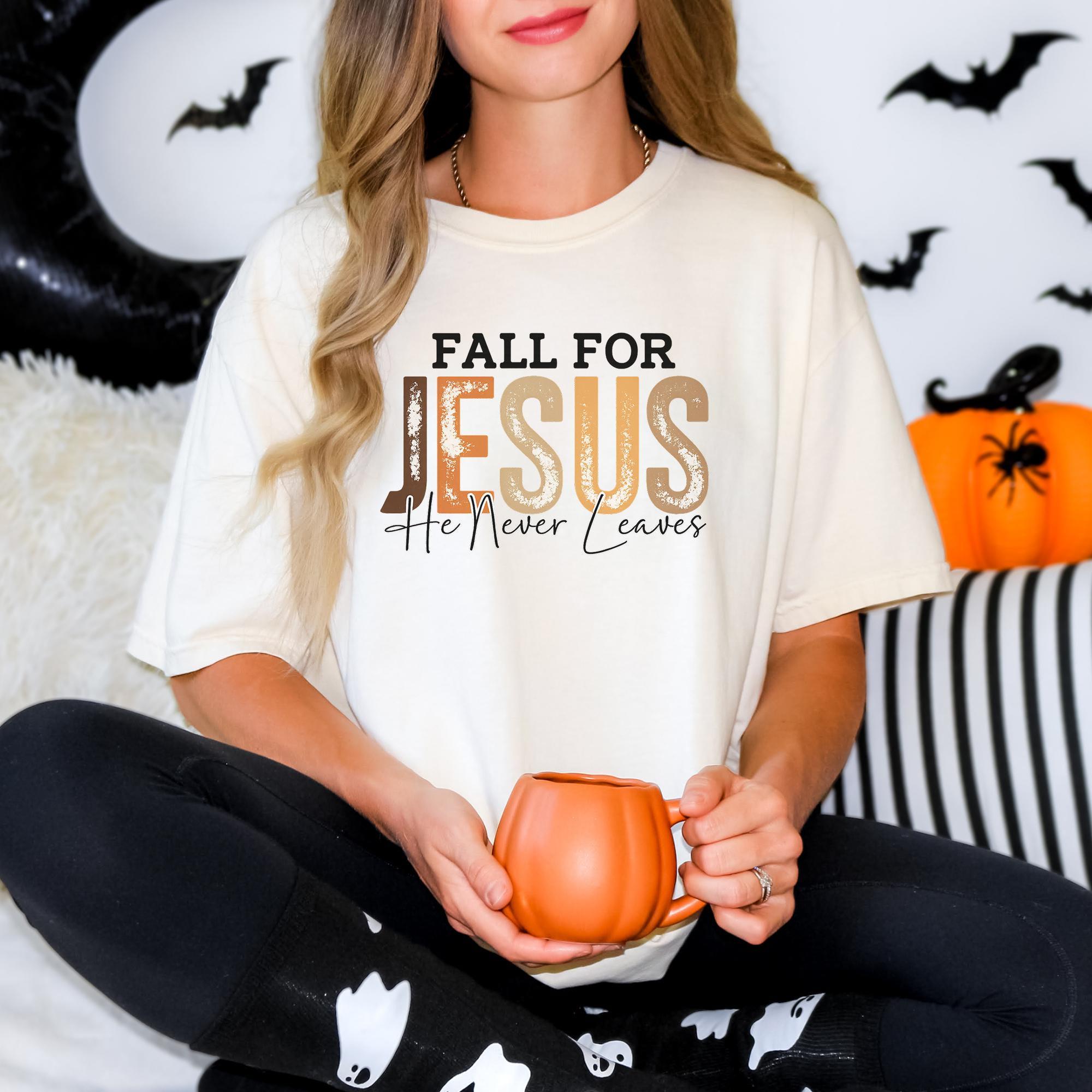 A woman wearing a white t-shirt with the text "FALL FOR JESUS He Never Leaves" is sitting on a couch, holding a pumpkin-shaped mug.