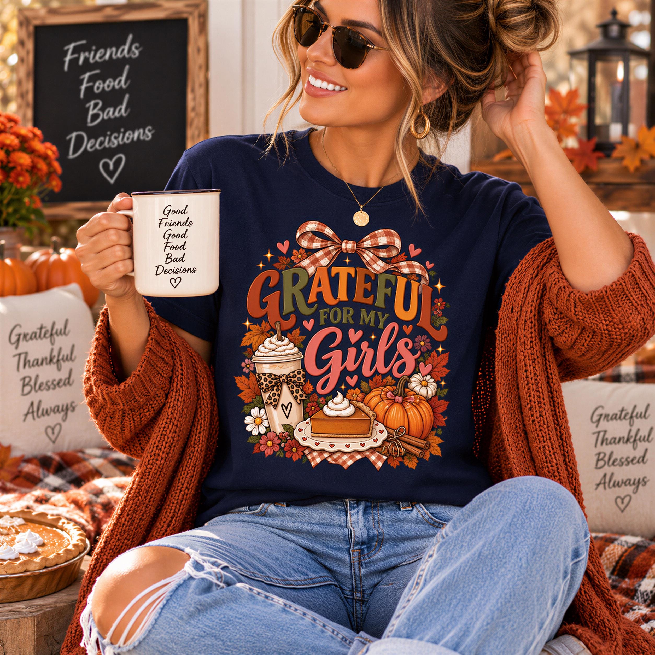 A woman wearing a blue t-shirt with a graphic design and holding a coffee mug, sitting in a cozy setting with fall decorations and a chalkboard sign.