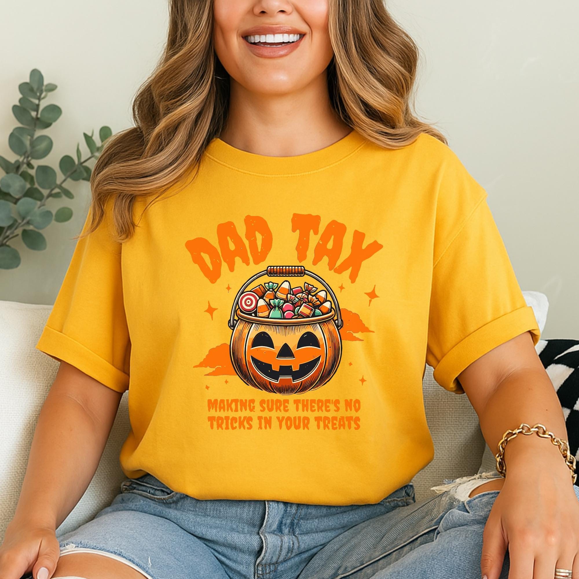 A woman wearing a yellow t-shirt with a graphic of a jack-o-lantern and the text "DAD TAX" and "Making sure there's no tricks in your treats" printed on it.