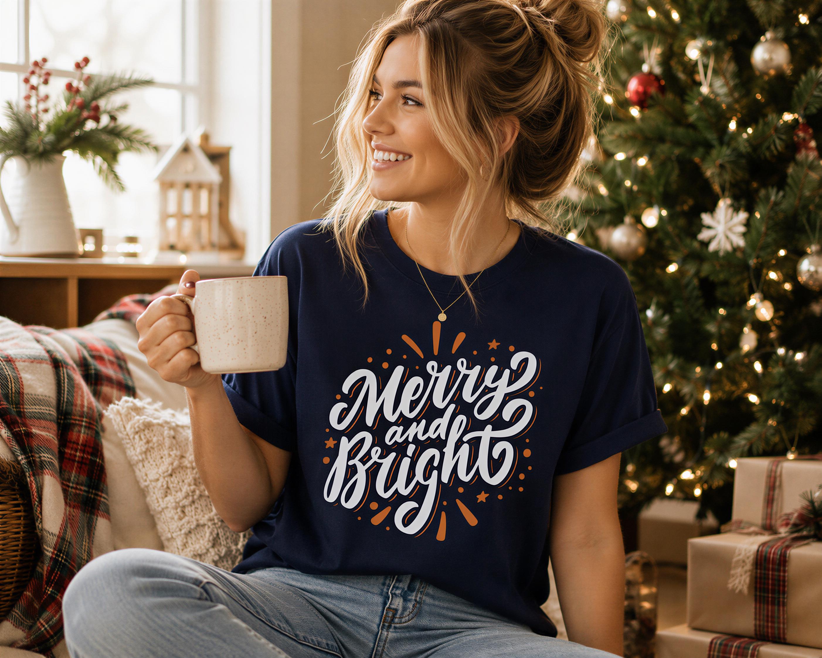 A woman sitting on a couch, holding a mug and wearing a blue t-shirt with the text "Merry and Bright" in a cozy, festive setting with a Christmas tree and holiday decorations.