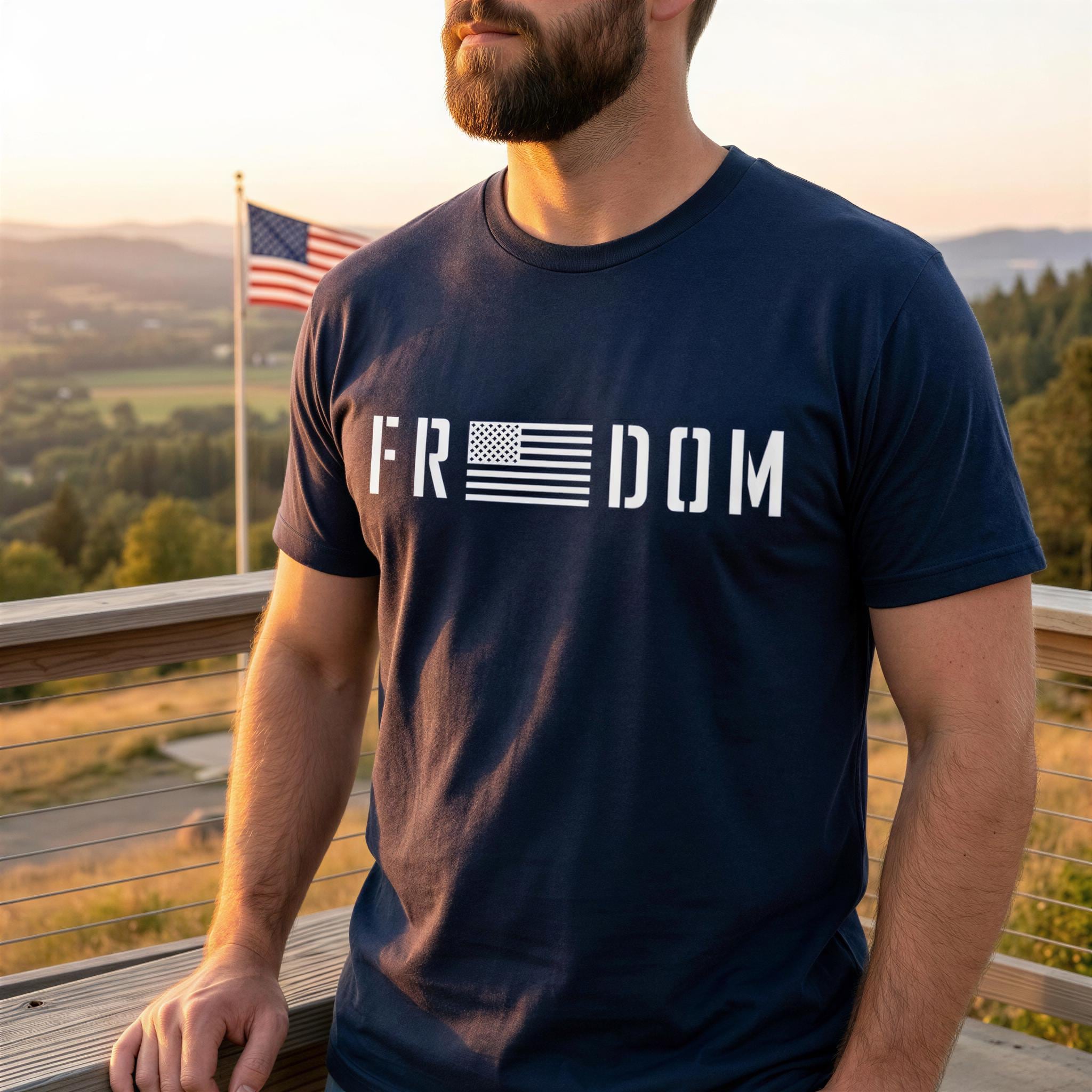 A man wearing a navy blue t-shirt with the word "FREEDOM" printed on it stands on a wooden platform, with an American flag visible in the background.