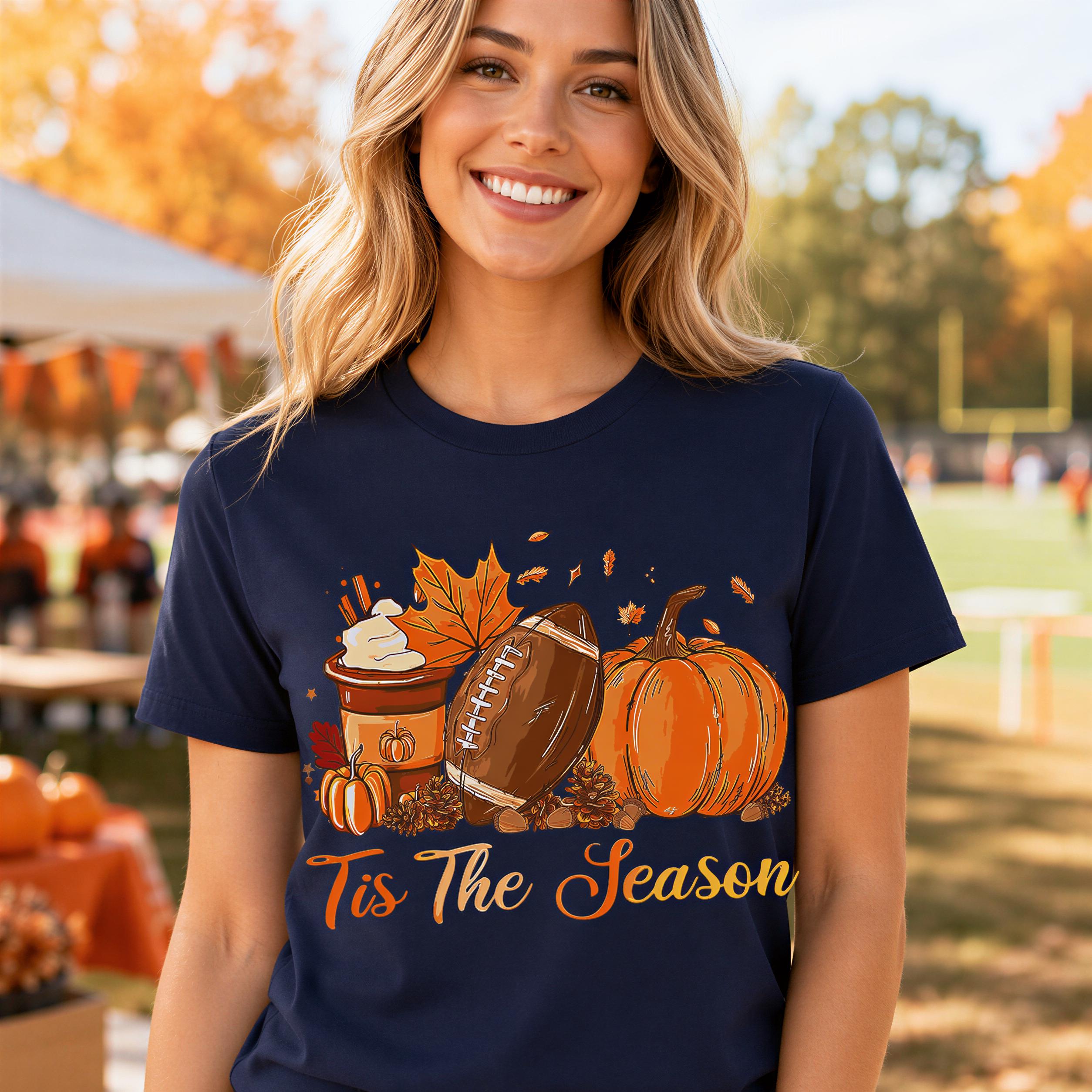 A smiling woman wearing a navy blue t-shirt with a graphic design of a football, pumpkins, and a cup of coffee, along with the text "Tis The Season".