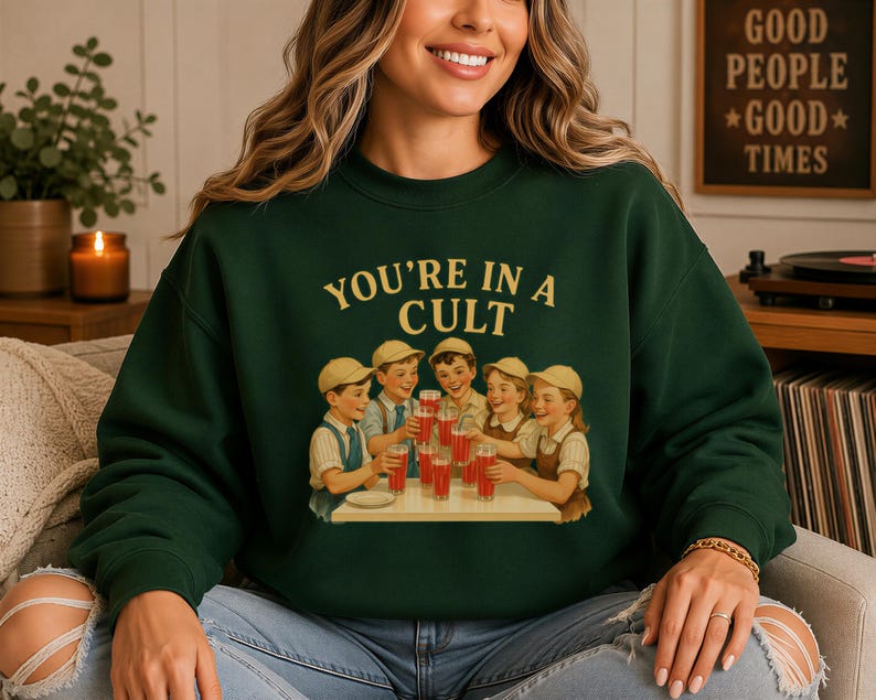A woman wearing a green sweatshirt with a graphic design of a group of people enjoying drinks at a table.