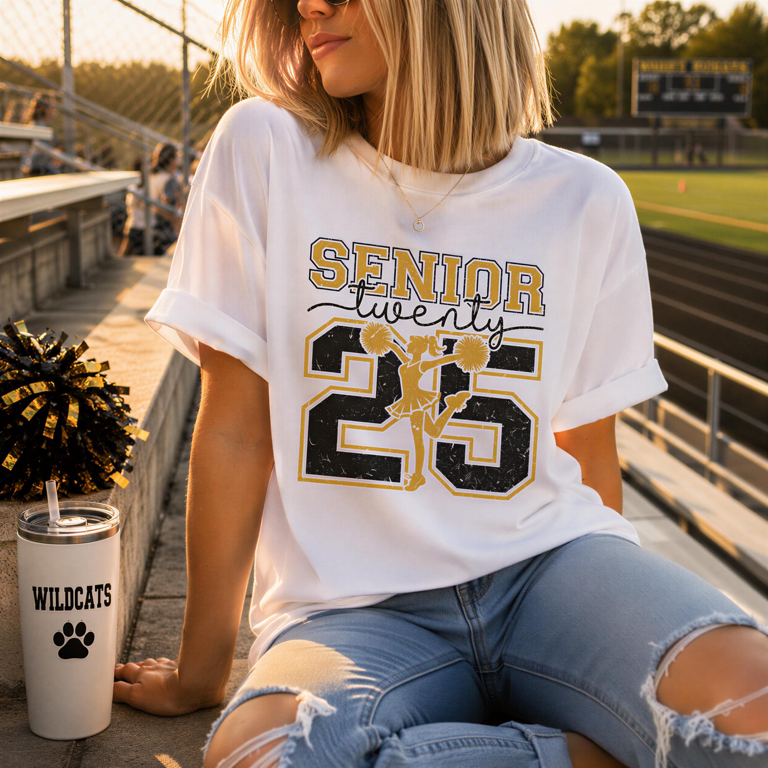 A woman wearing a white t-shirt with a cheerleader design and the number 25, sitting on a bleachers with a pom pom and a cup of what appears to be a beverage.