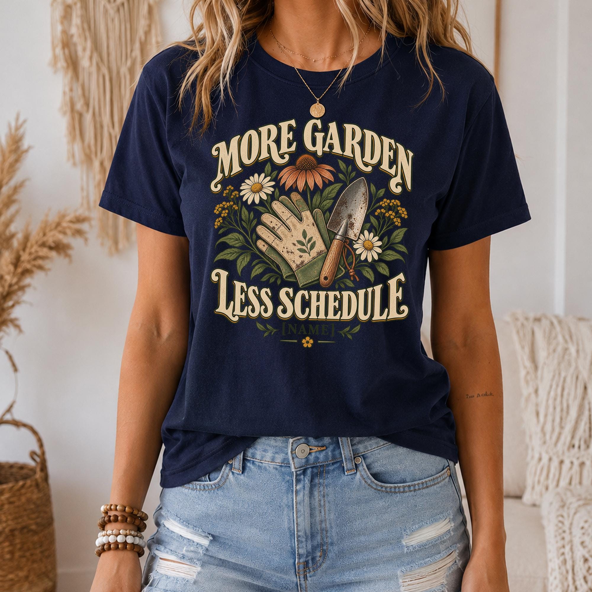 A woman wearing a navy blue t-shirt with a graphic design that says "MORE GARDEN LESS SCHEDULE" and includes a hand holding a gardening tool and flowers.