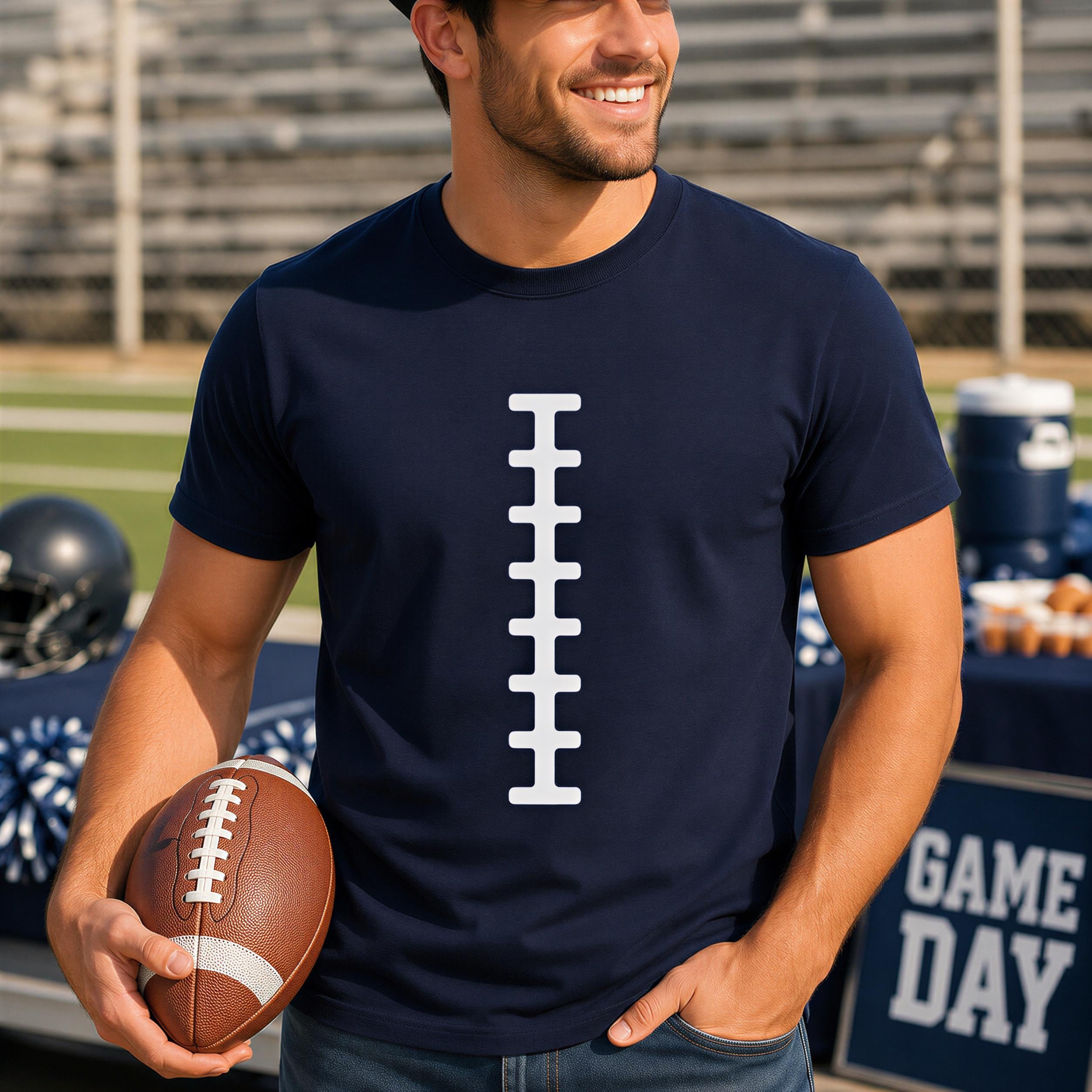 A man wearing a navy blue t-shirt with a white football design is holding a football and smiling at the camera.