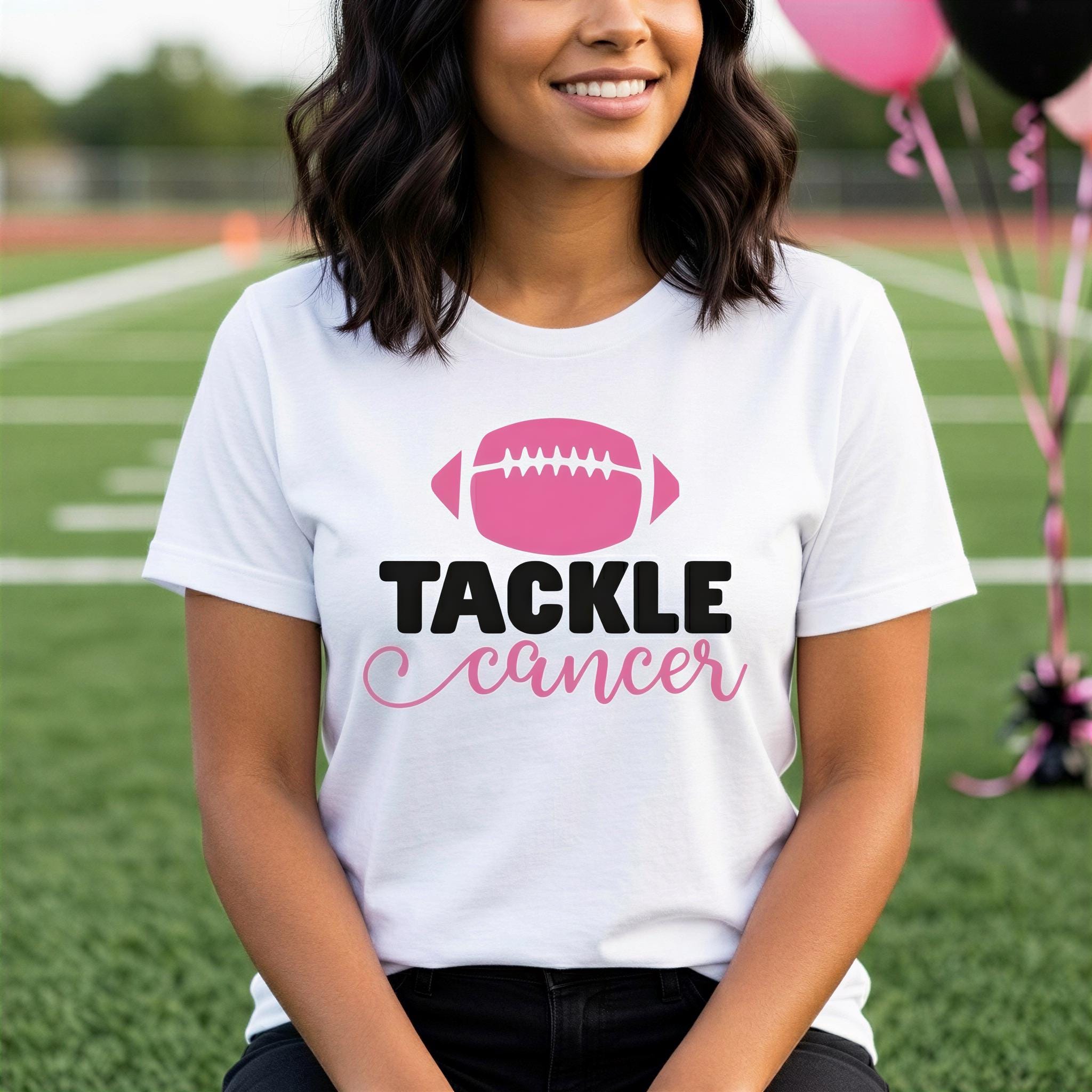 A woman wearing a white t-shirt with a pink football graphic and the text "TACKLE CANCER" is standing on a grassy field.