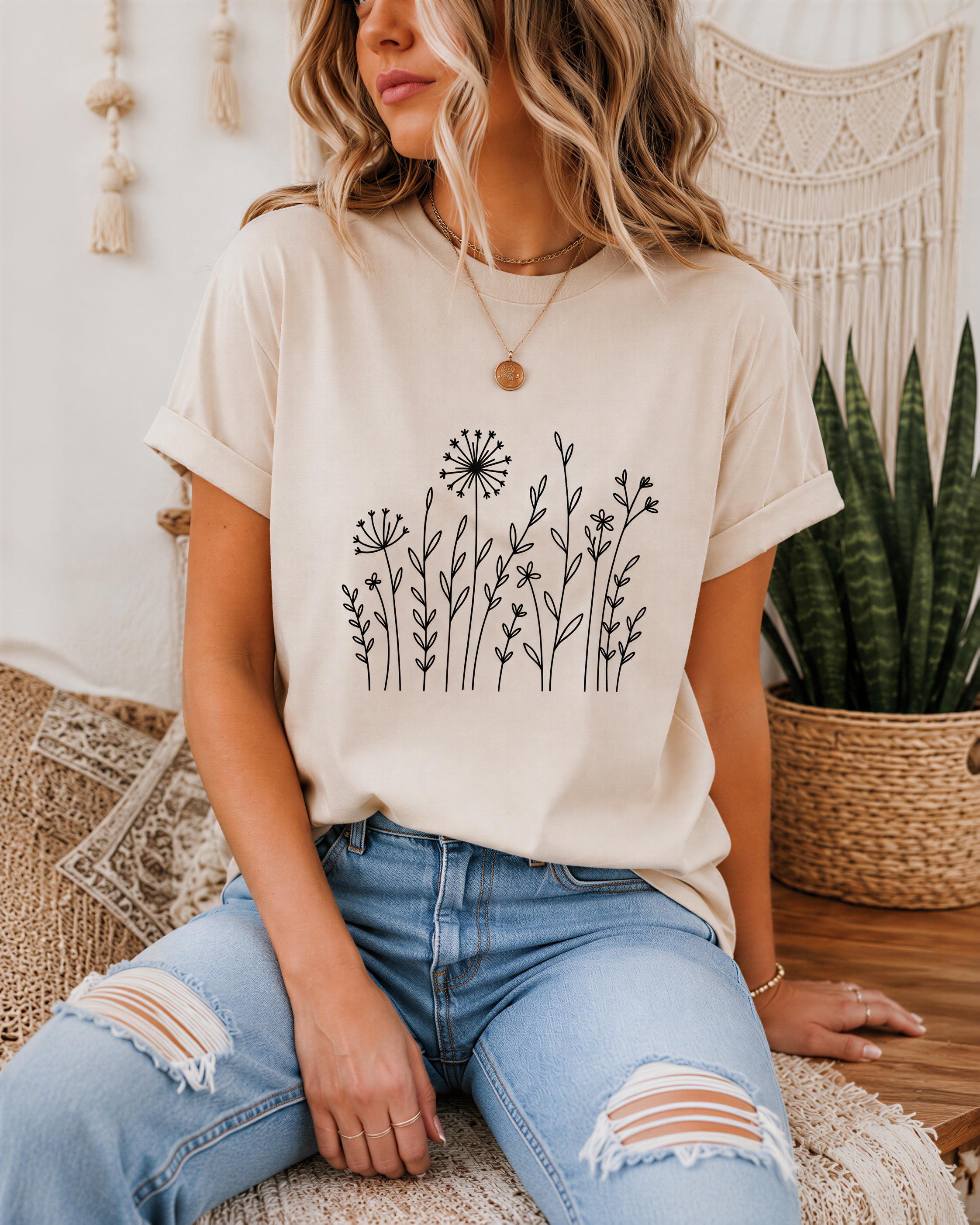 A woman wearing a beige t-shirt with a floral design and distressed blue jeans is sitting on a woven chair.