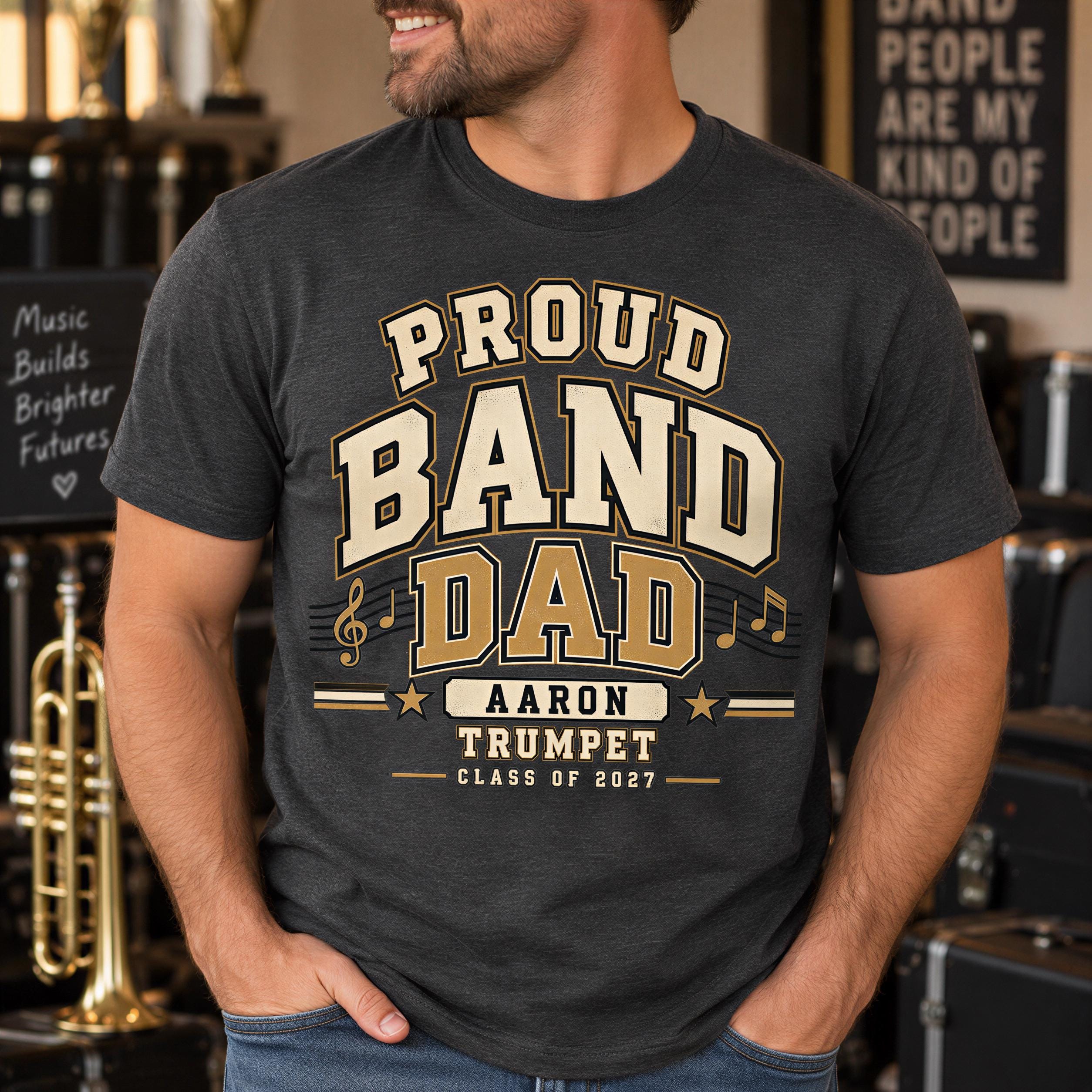 A man wearing a black t-shirt with a graphic design that says "Proud Band Dad Aaron Trumpet Class of 2017".