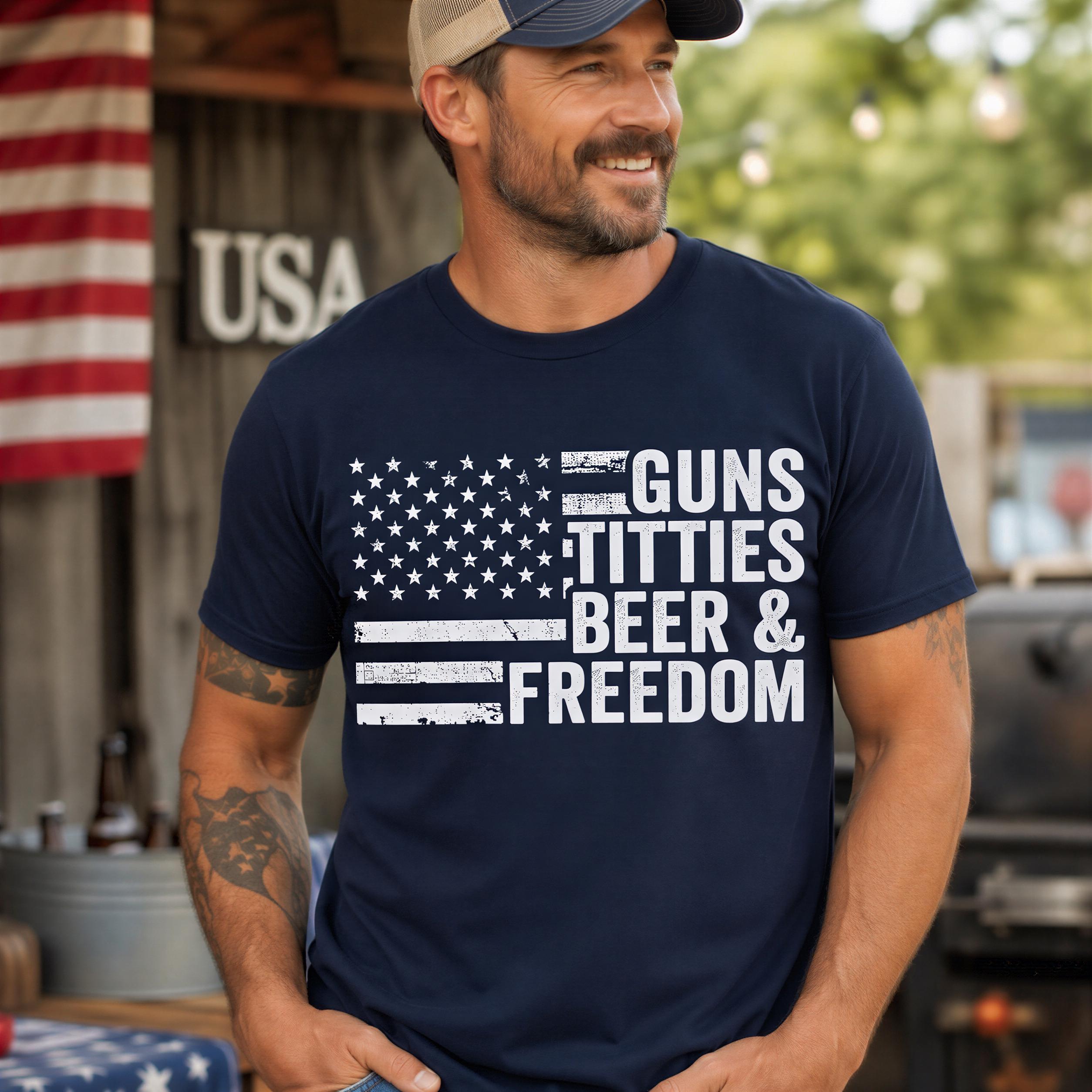 A man wearing a navy blue t-shirt with the text "GUNS TITTIES BEER & FREEDOM" printed on it, standing in front of an American flag.