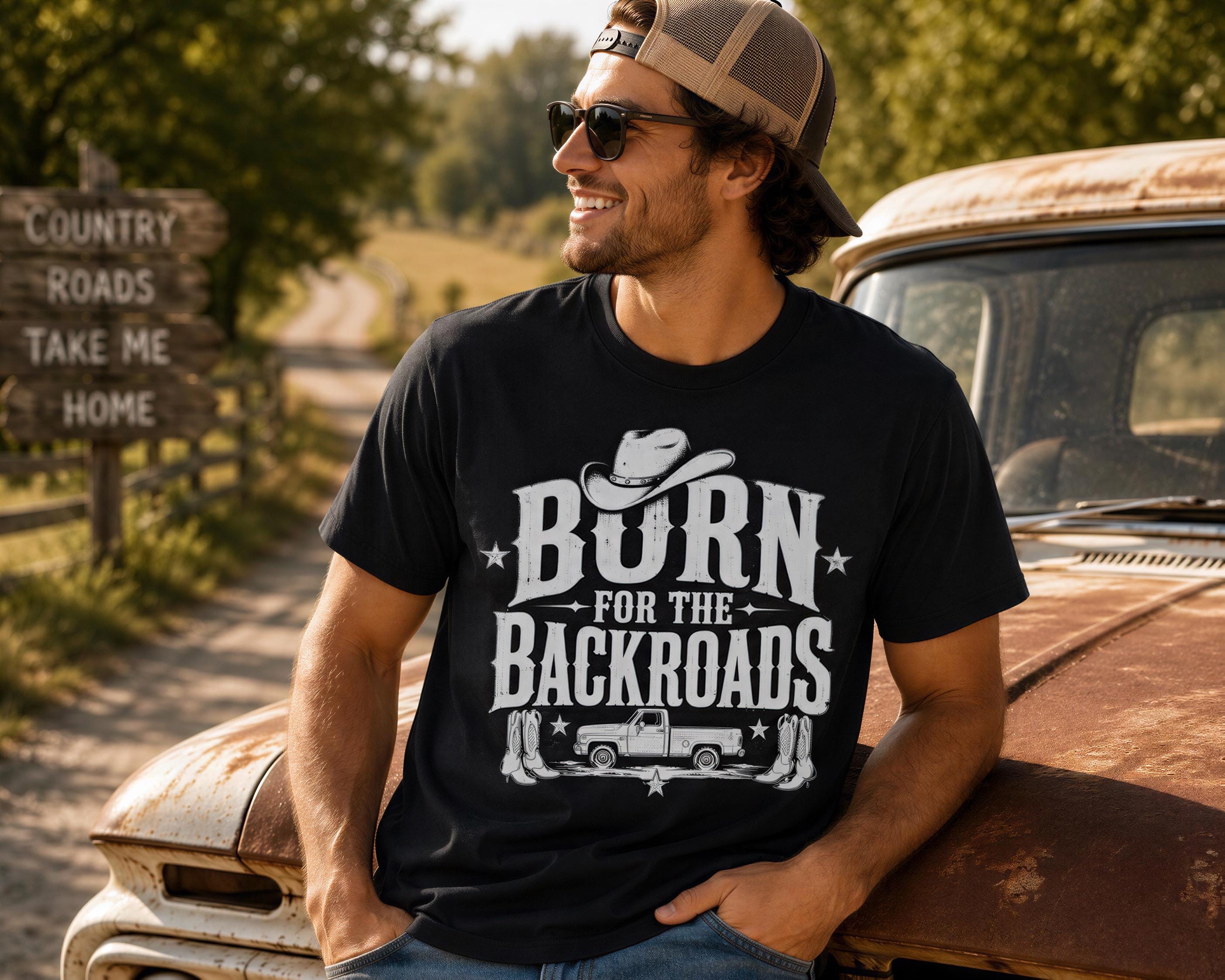 A man wearing a black t-shirt with a cowboy hat and sunglasses is leaning on an old, rusted truck in a rural setting.