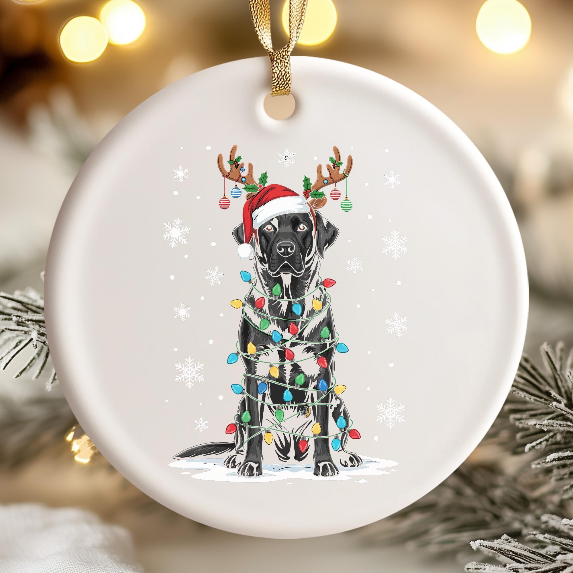 A white ornament with a black dog wearing a Santa hat and antlers, surrounded by colorful Christmas lights.