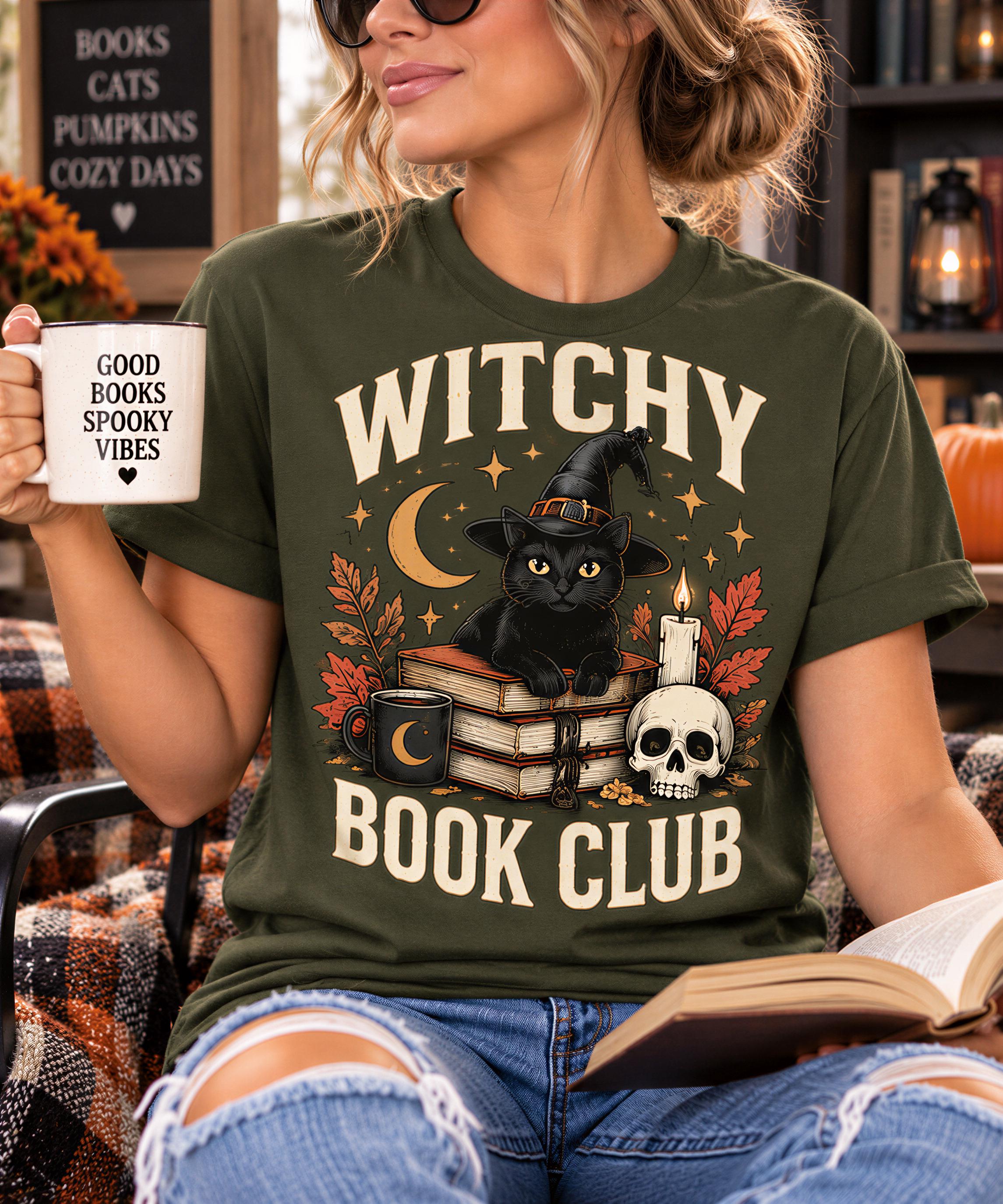 A woman wearing a green t-shirt with a graphic design of a black cat, a skull, and autumn leaves, holding a mug with the text "GOOD BOOKS SPOOKY VIBES" and "WITCHY BOOK CLUB" printed on it.