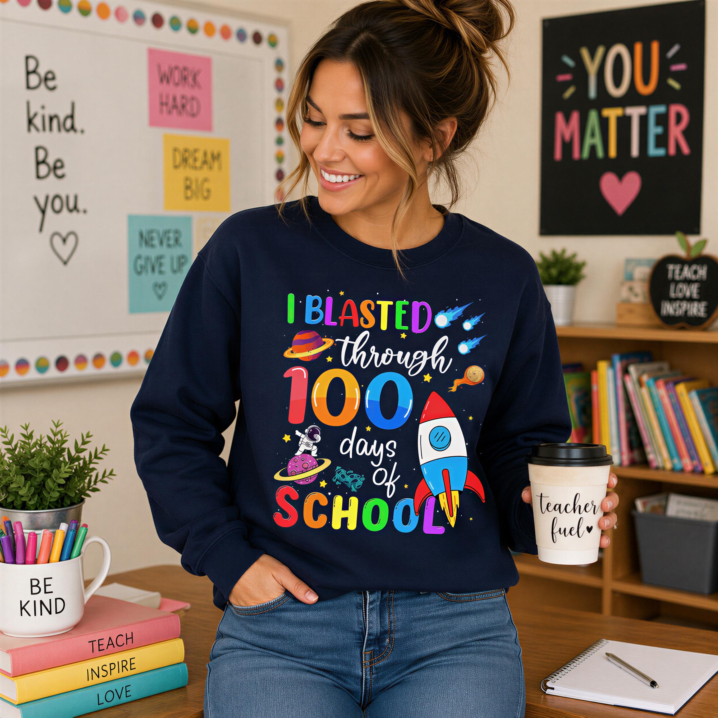 A woman wearing a blue sweatshirt with a colorful design and text, smiling and holding a coffee cup, standing in a classroom setting with bookshelves and a bulletin board in the background.