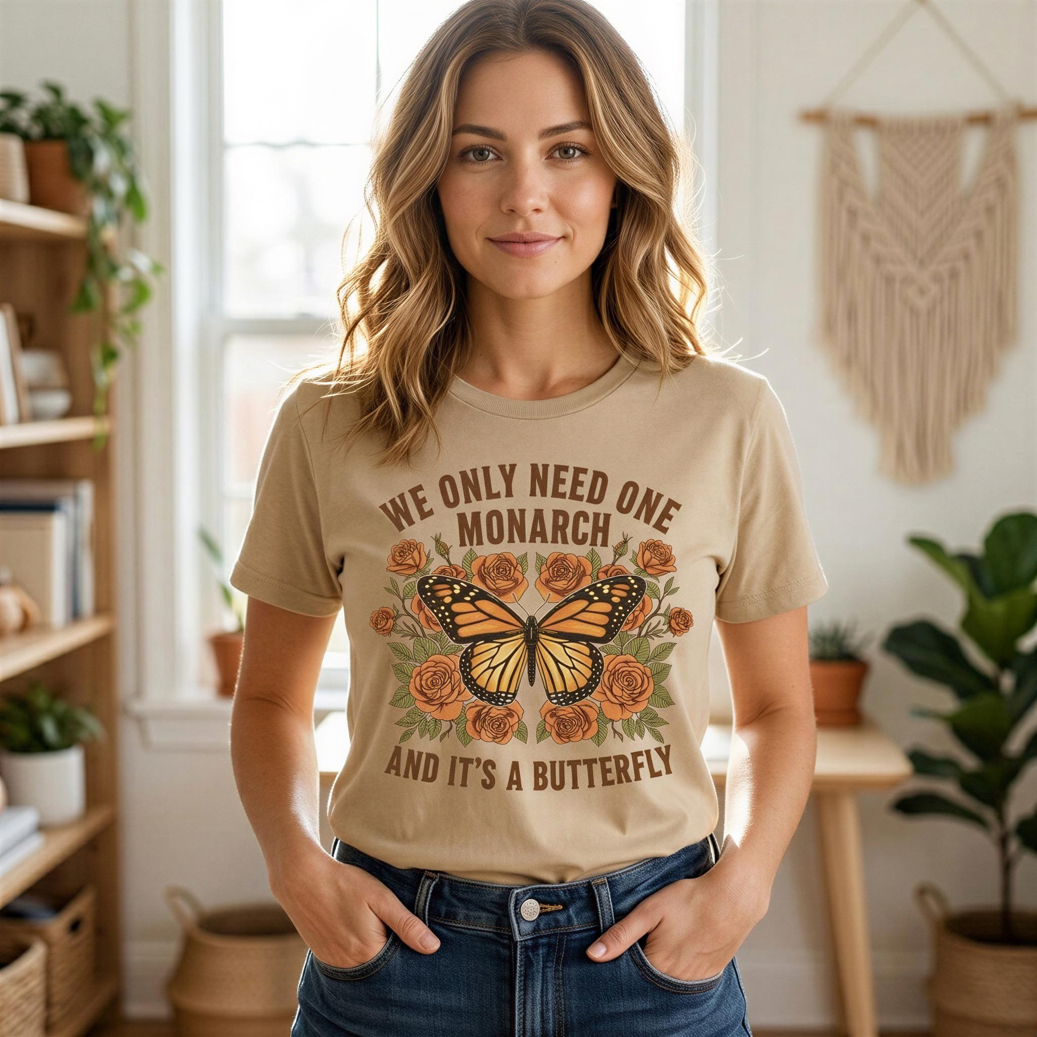 A woman wearing a beige t-shirt with a graphic of a butterfly and flowers, standing in a room with plants and a window.
