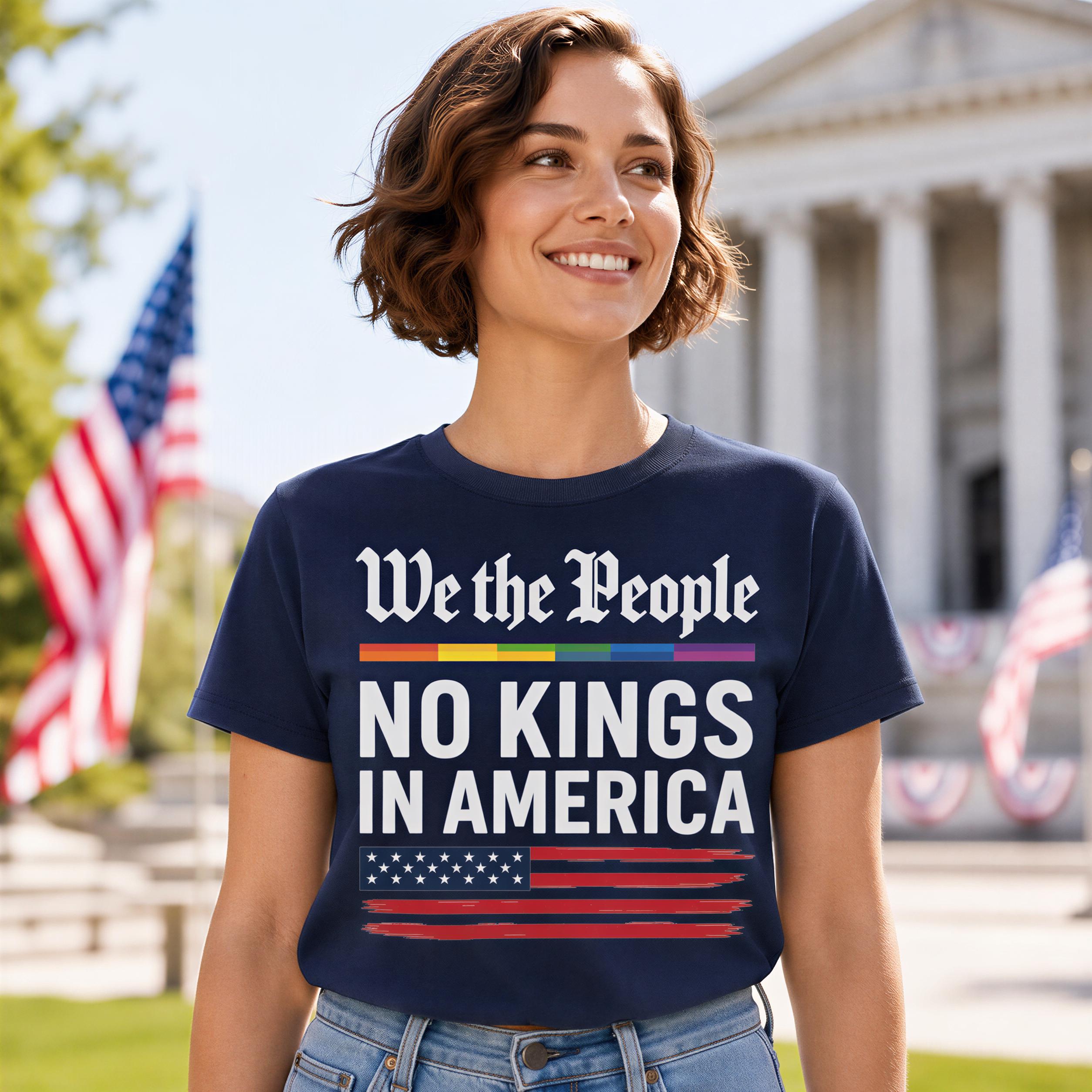 A woman wearing a navy blue t-shirt with the text "We the People NO KINGS IN AMERICA" stands in front of a building with an American flag.
