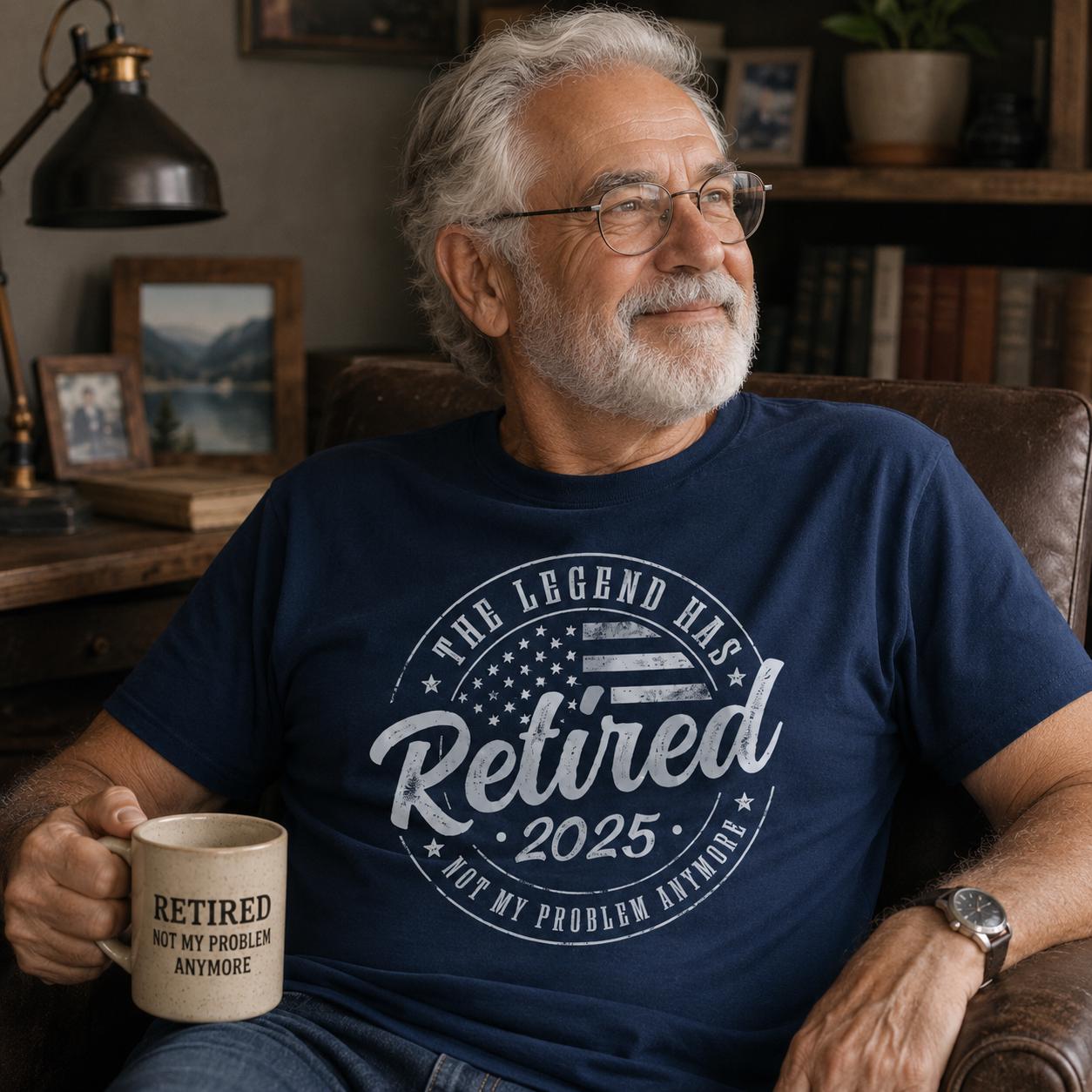 An older man with a beard and glasses is sitting in a chair, holding a coffee mug and wearing a blue t-shirt with a humorous text printed on it.