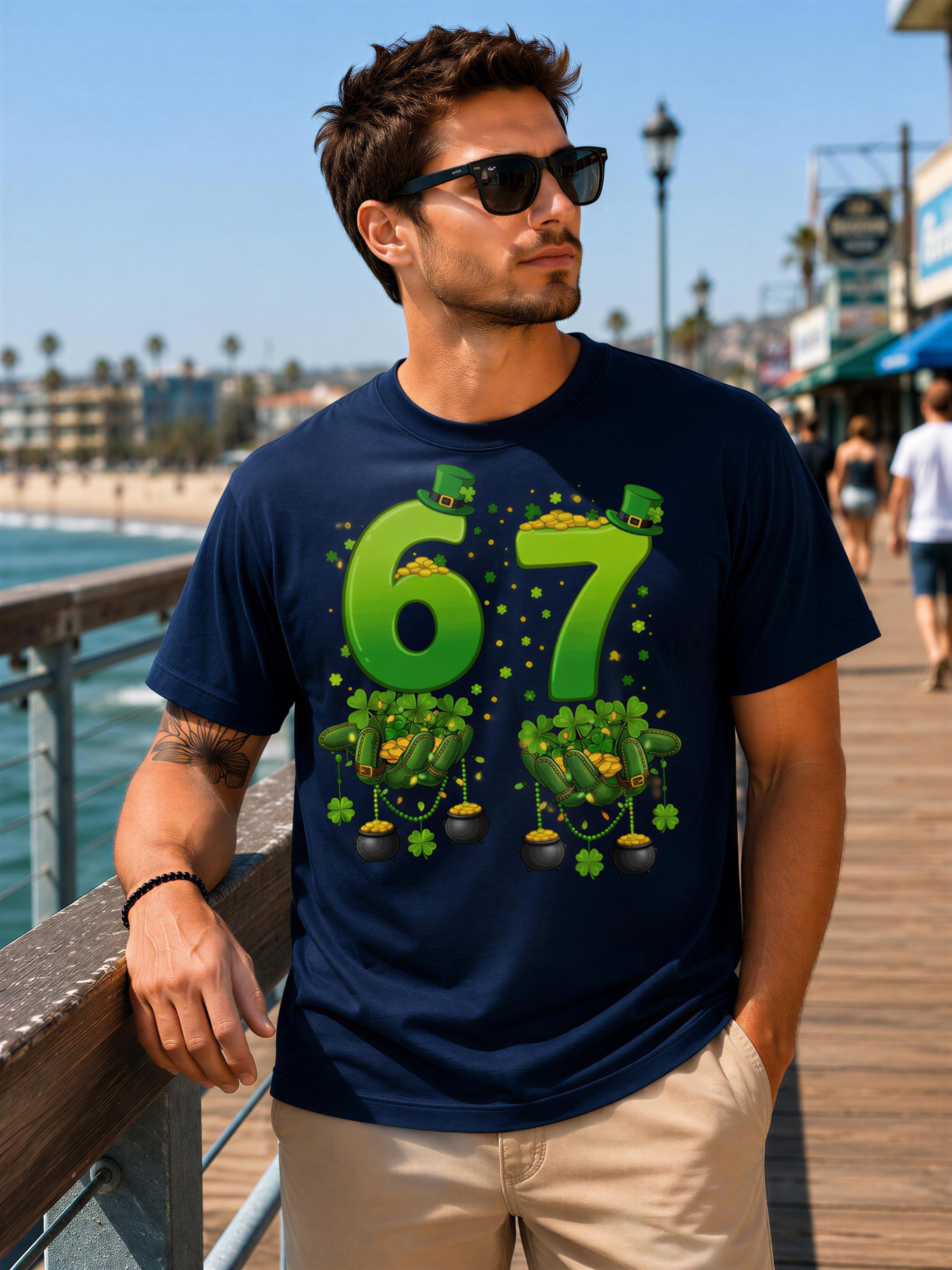 A man wearing a navy blue t-shirt with a graphic design of green numbers and shamrocks, standing on a pier overlooking the ocean.
